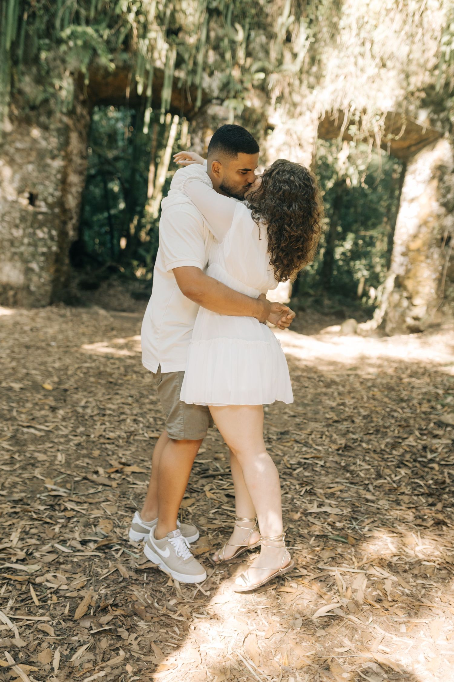 A couple in white and khaki embraces on a woodland path.