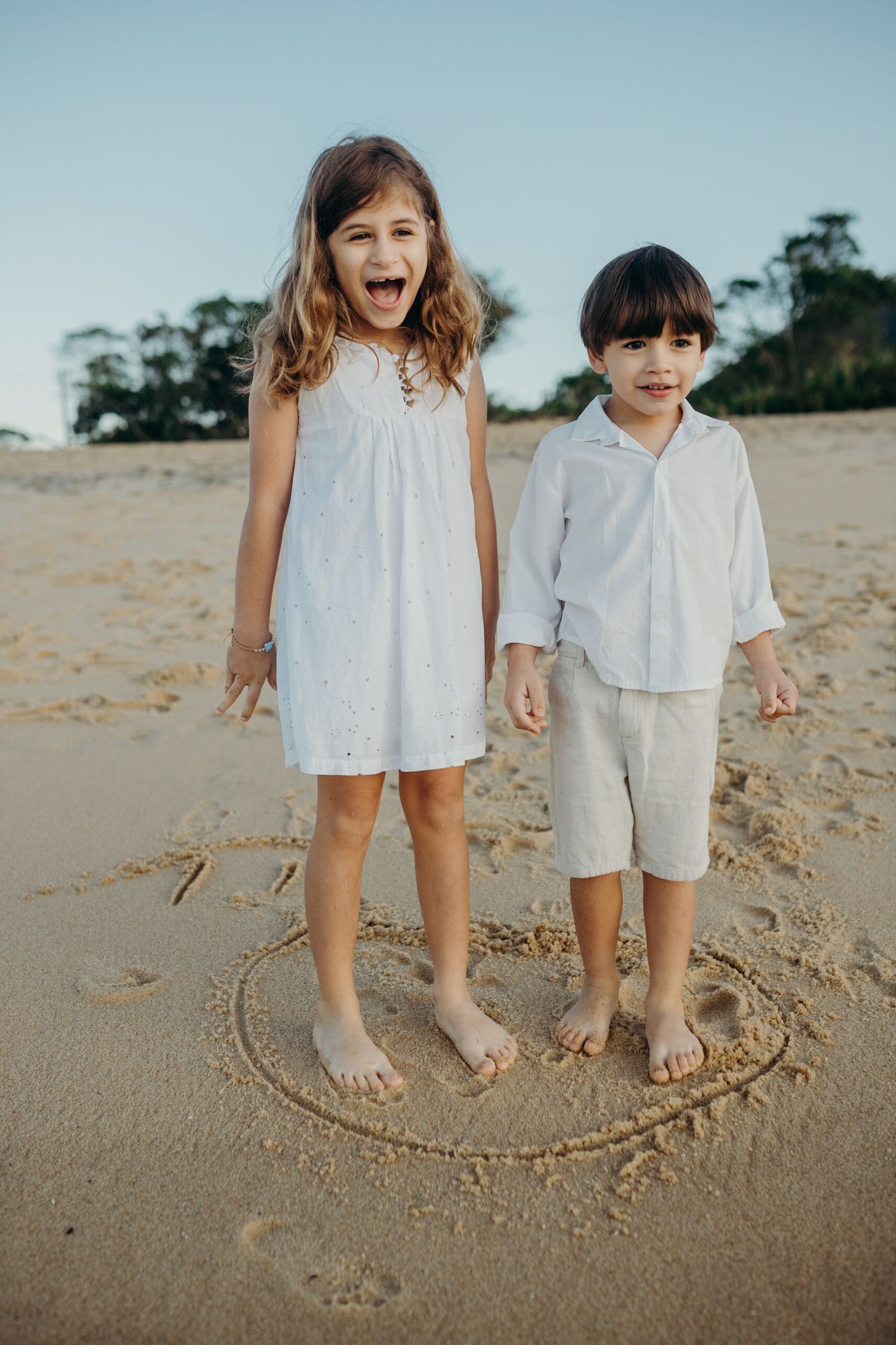 Children's feet stand inside a heart drawn in the sand on a sunny beach.