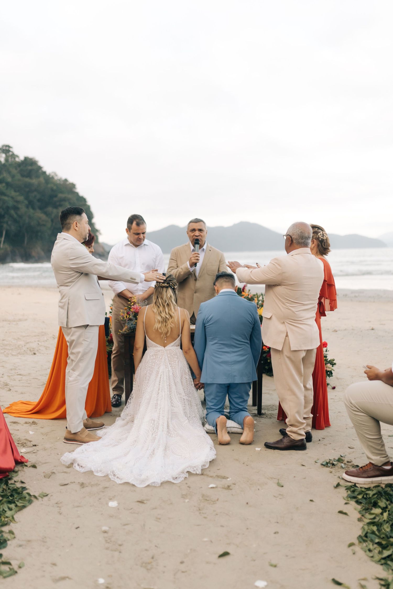 Wedding ceremony on a scenic beach with guests and newlyweds standing against a mountainous coastal backdrop.