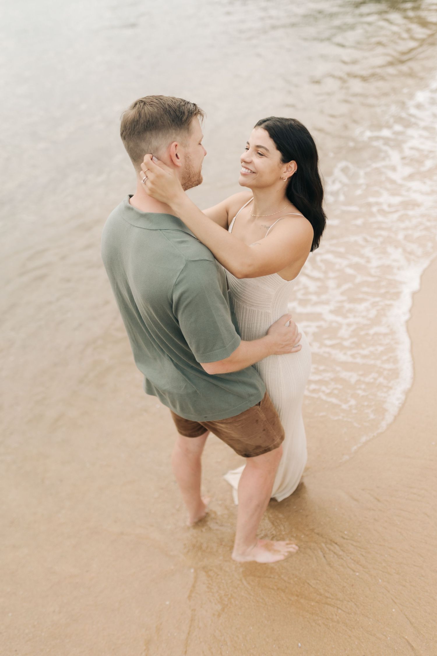 A loving couple shares an intimate moment while standing in the shallow waters of a beach.