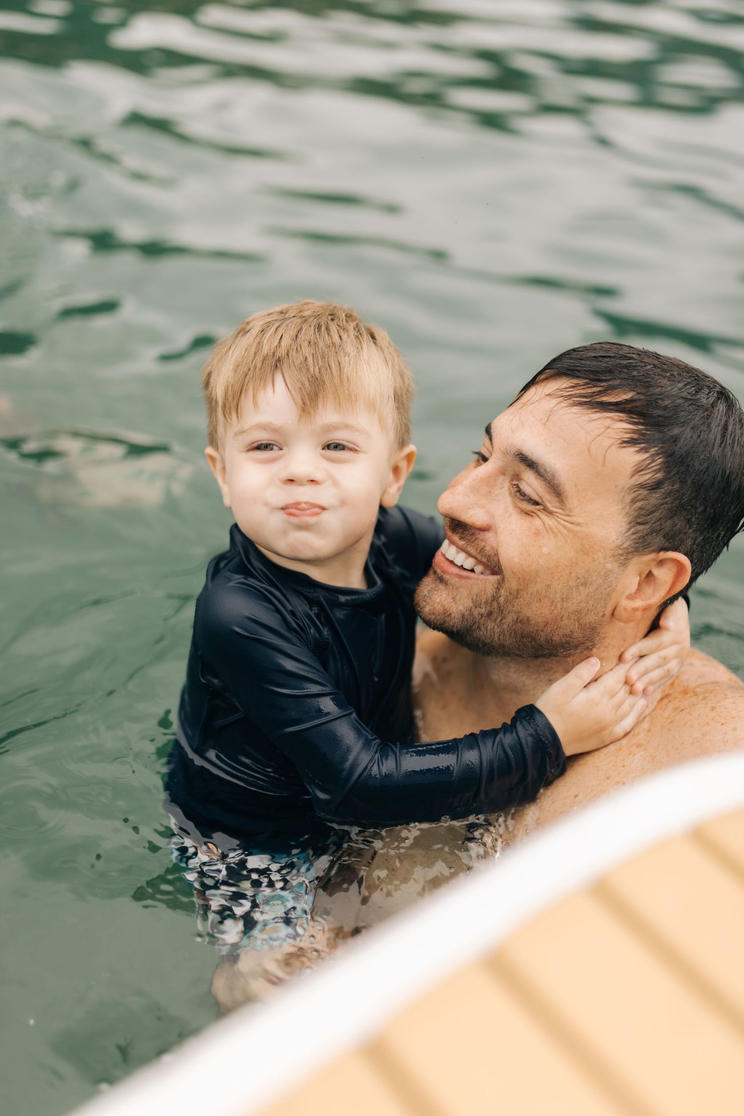 Tender parent-child bonding moment while swimming together near boat deck.