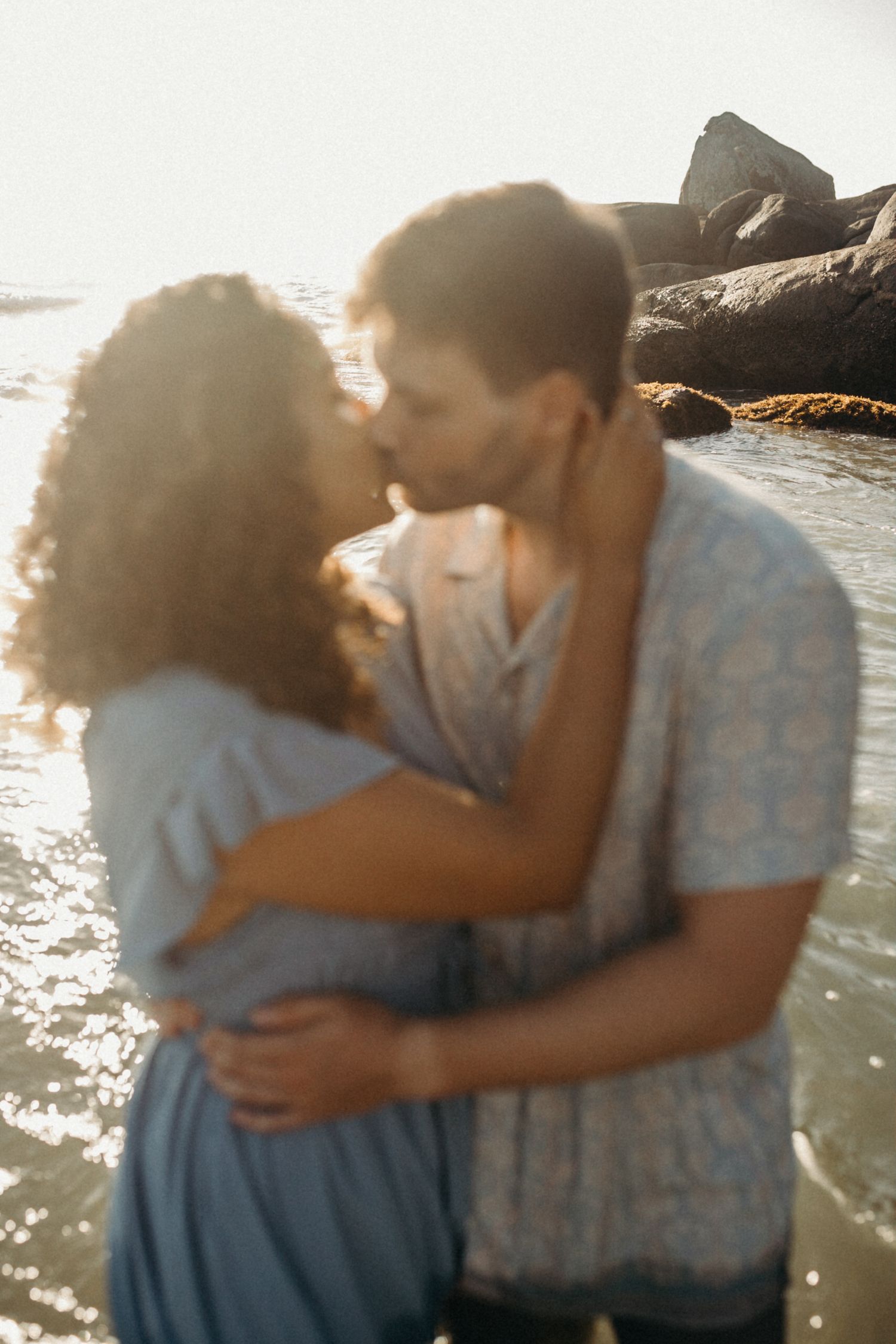 Couple sharing tender embrace while standing in shallow ocean water during golden hour.