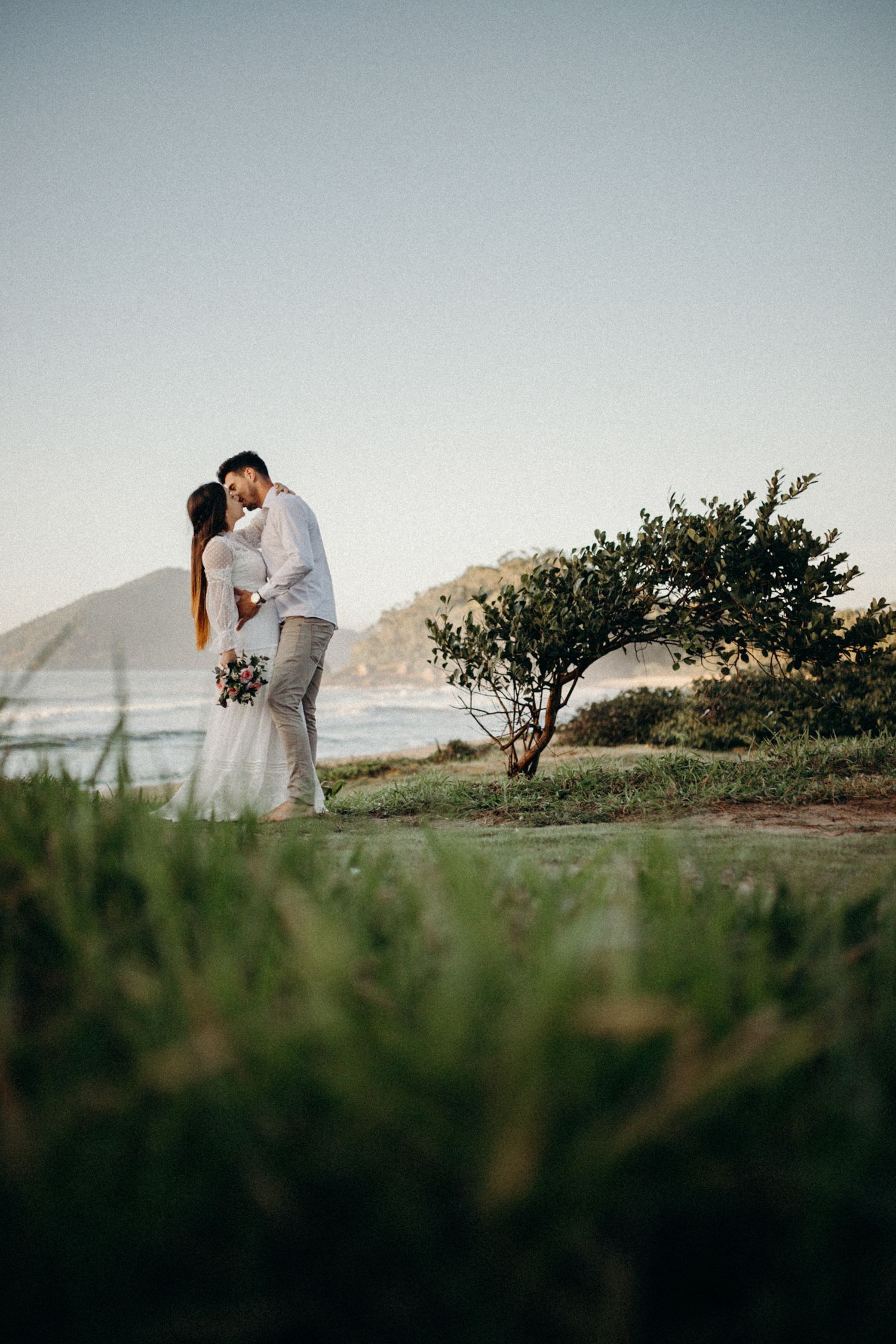 A couple shares an intimate moment on a coastal cliff with ocean views at sunset.