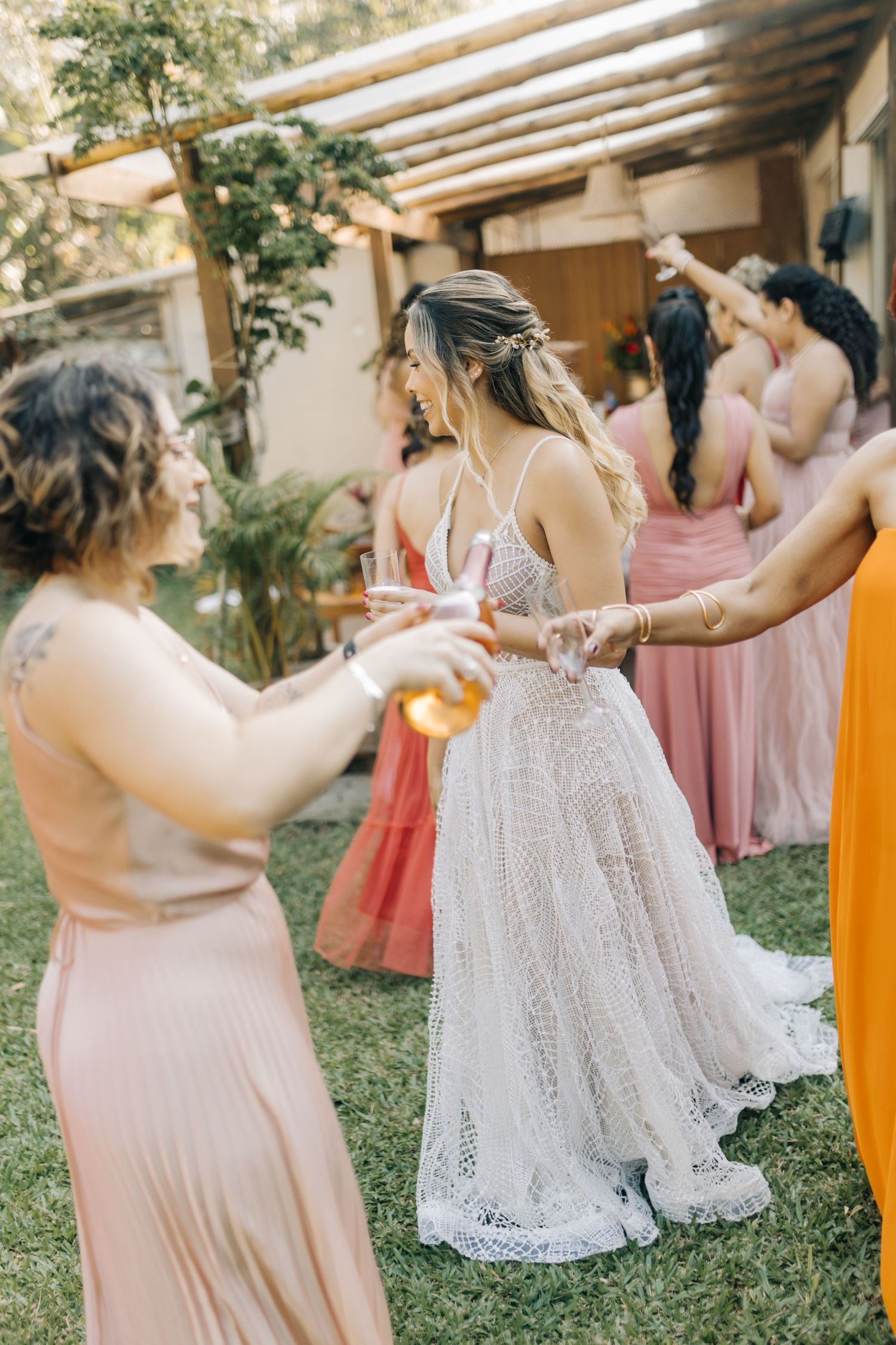 Wedding celebration under a pergola with attendees in formal dresses sharing drinks and laughter.