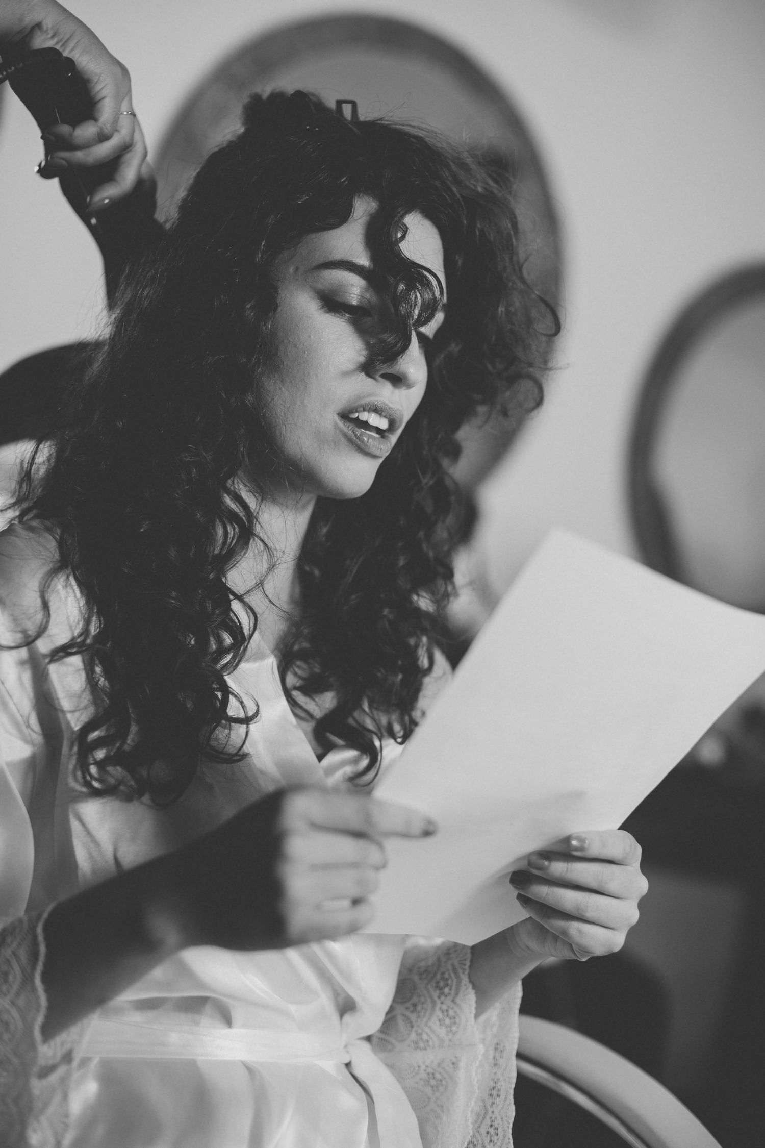 Black and white portrait of someone in white robe reading document with dramatic lighting.