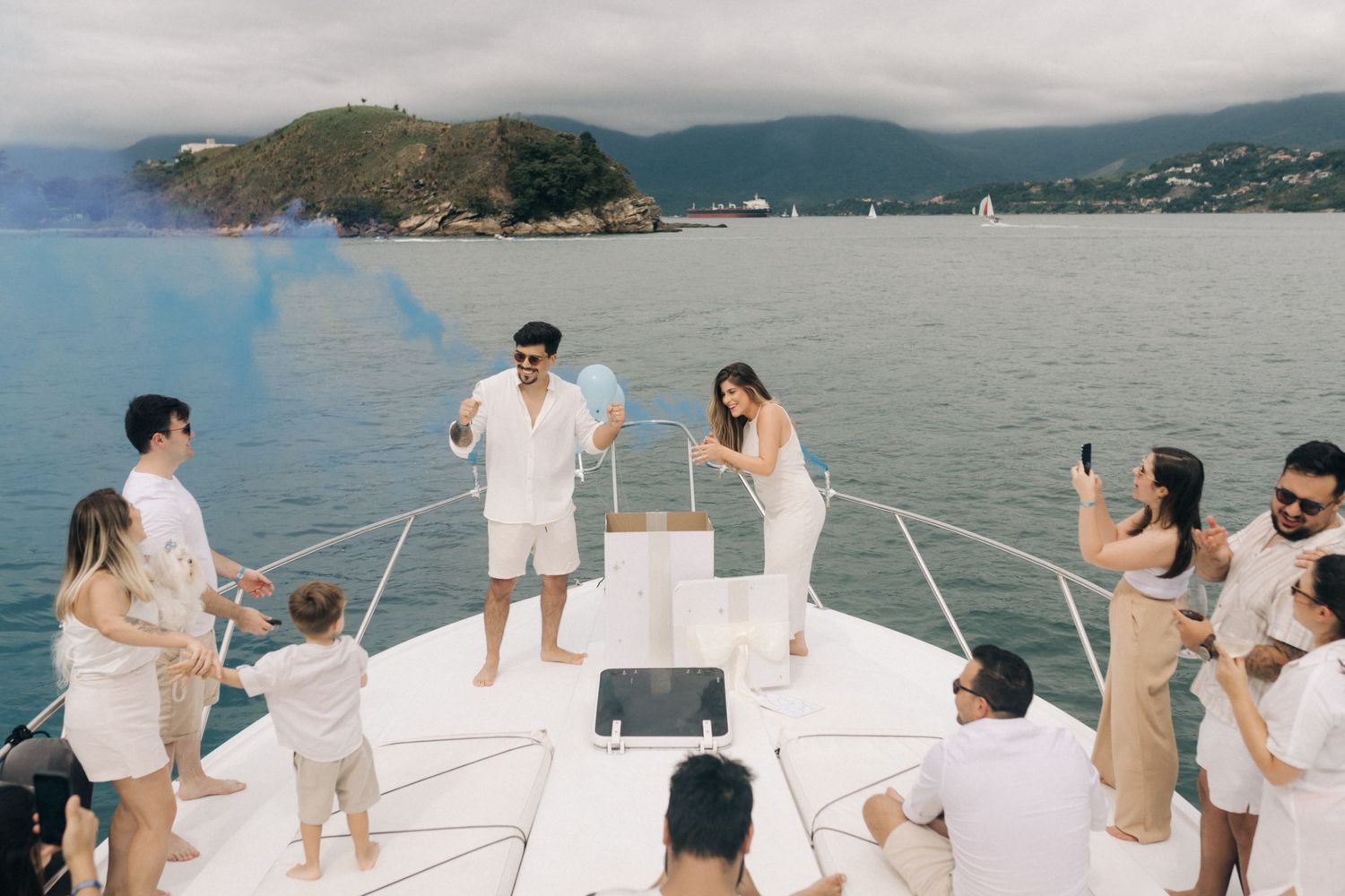 Friends gather on a yacht deck for a celebration with coastal scenery in the background.
