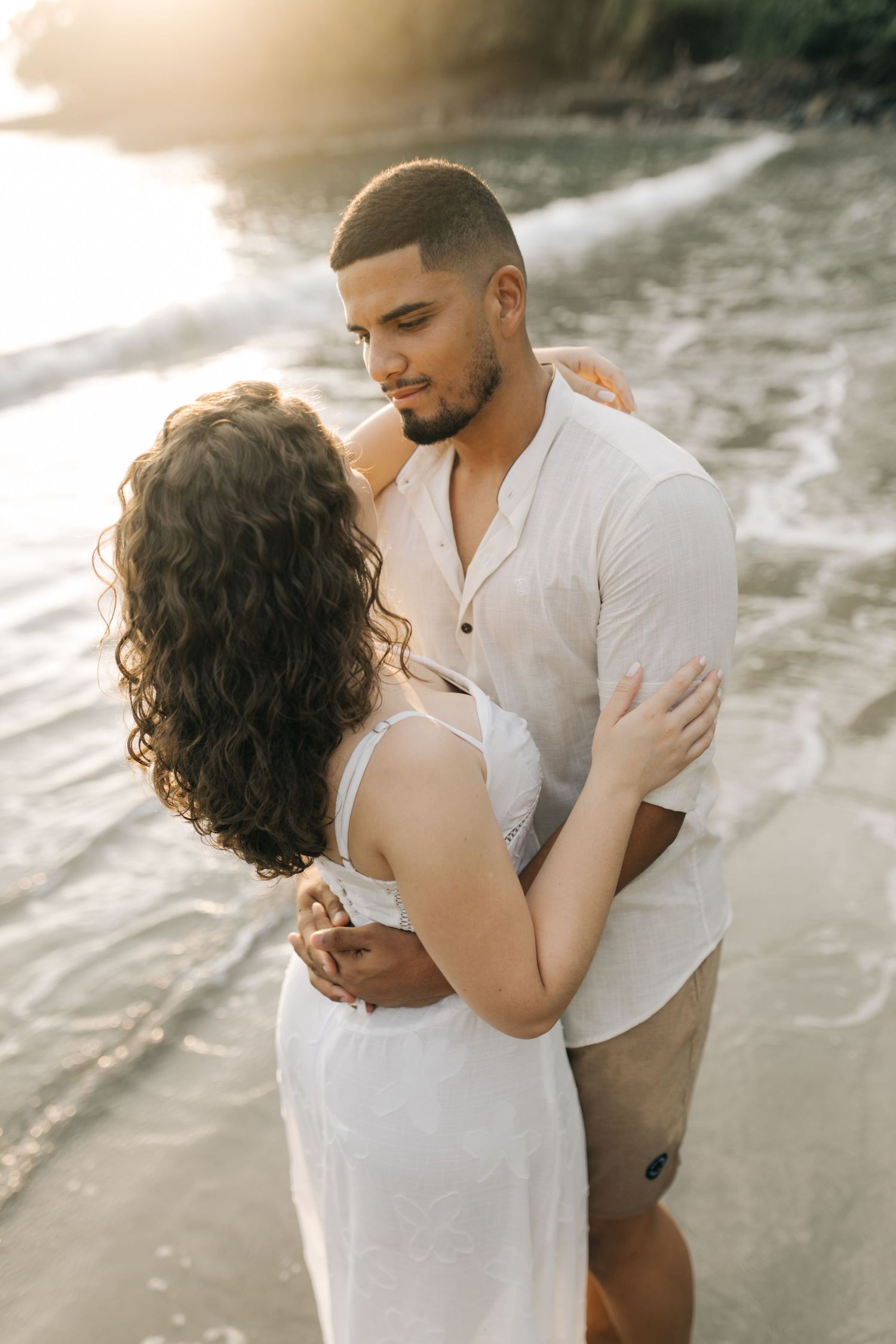 Couple shares intimate embrace during romantic beach photoshoot at sunset.