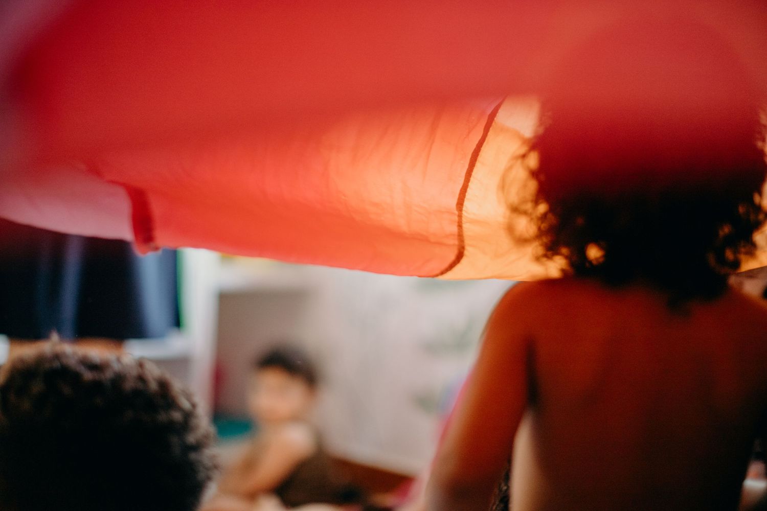 Blurred silhouettes against red and orange fabric in soft focus.