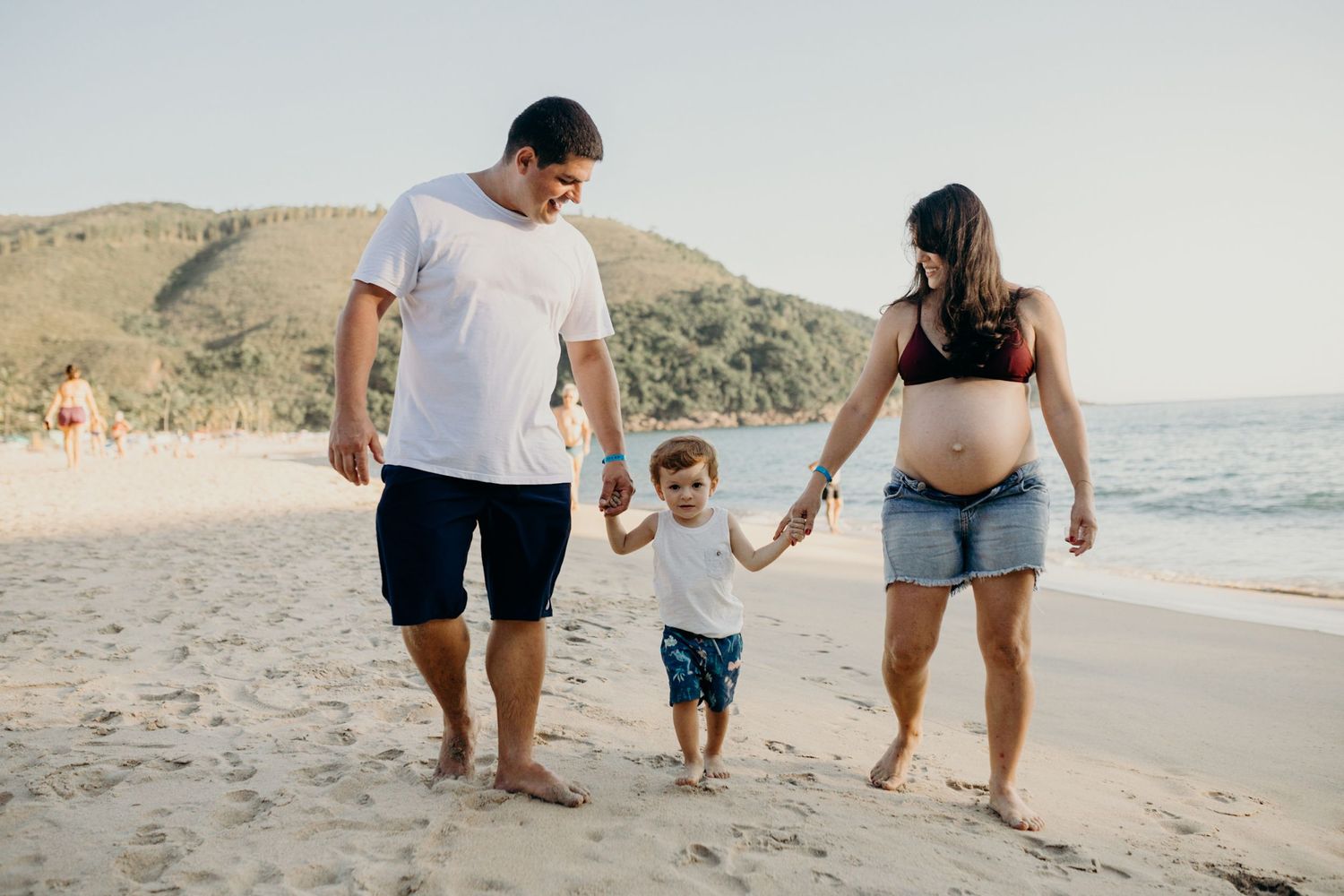 Family members walking together along shoreline at beach during golden hour.