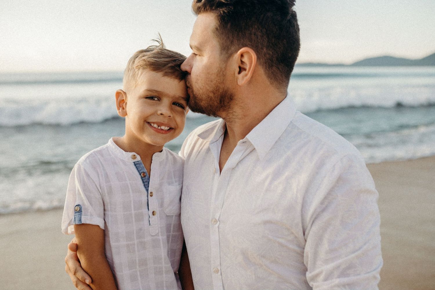 Sweet interaction between parent and child wearing white shirts on sunny beach.