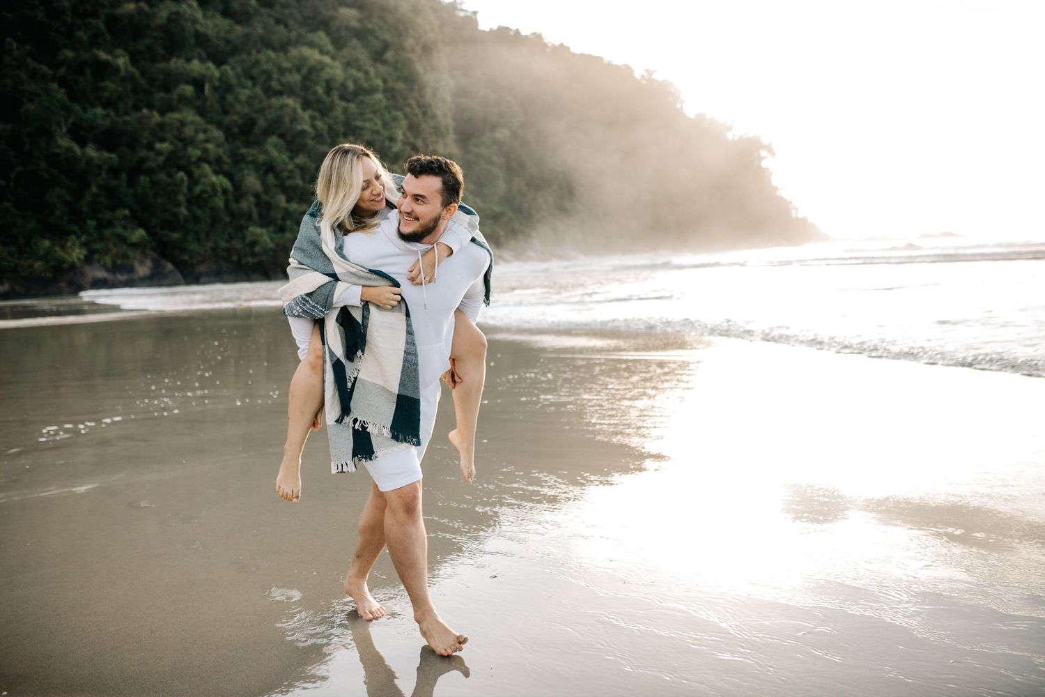 Romantic beach photoshoot with couple enjoying a piggyback ride along the shoreline.