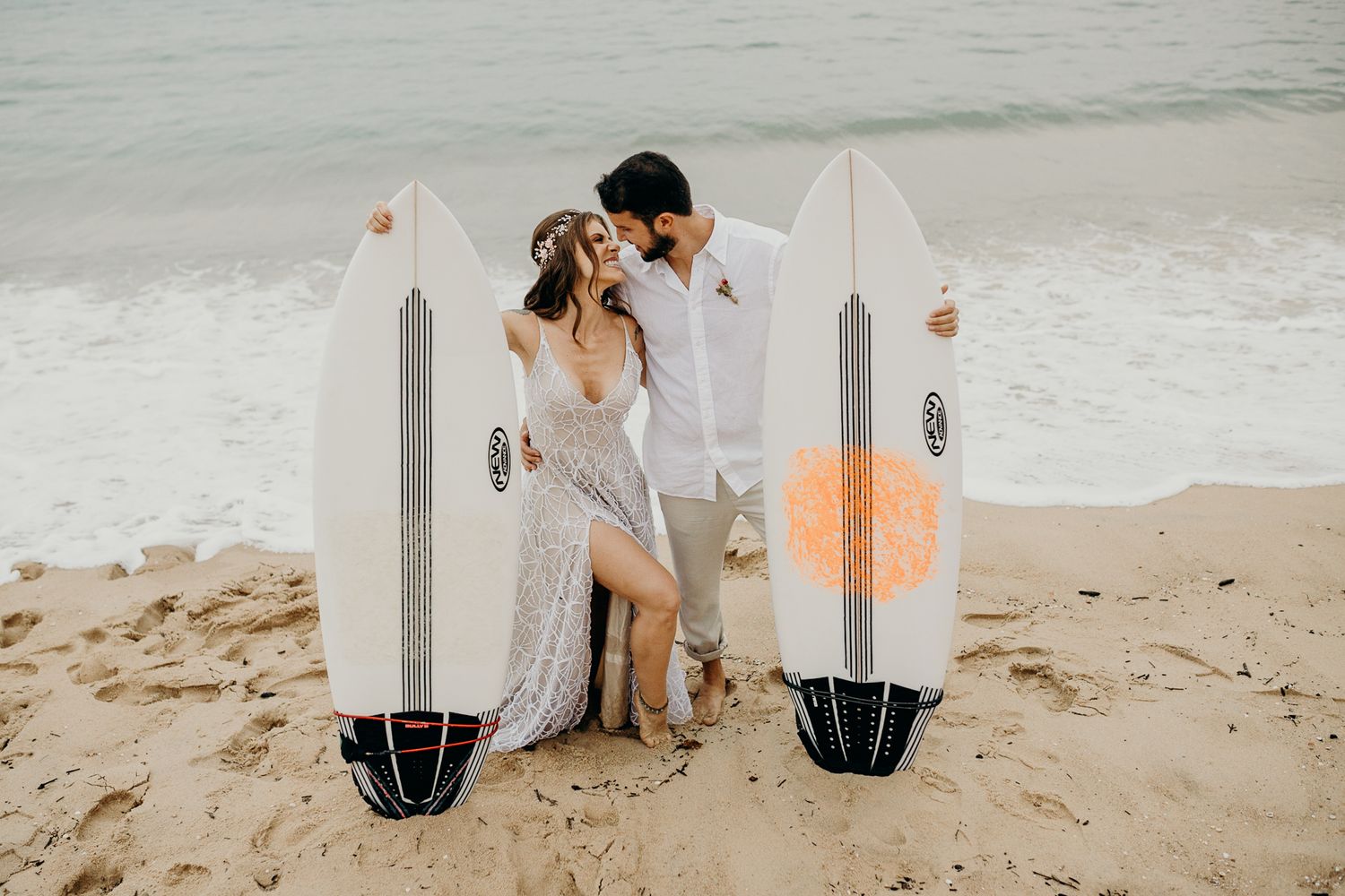 Couple sharing an intimate moment between two surfboards on a sandy beach.