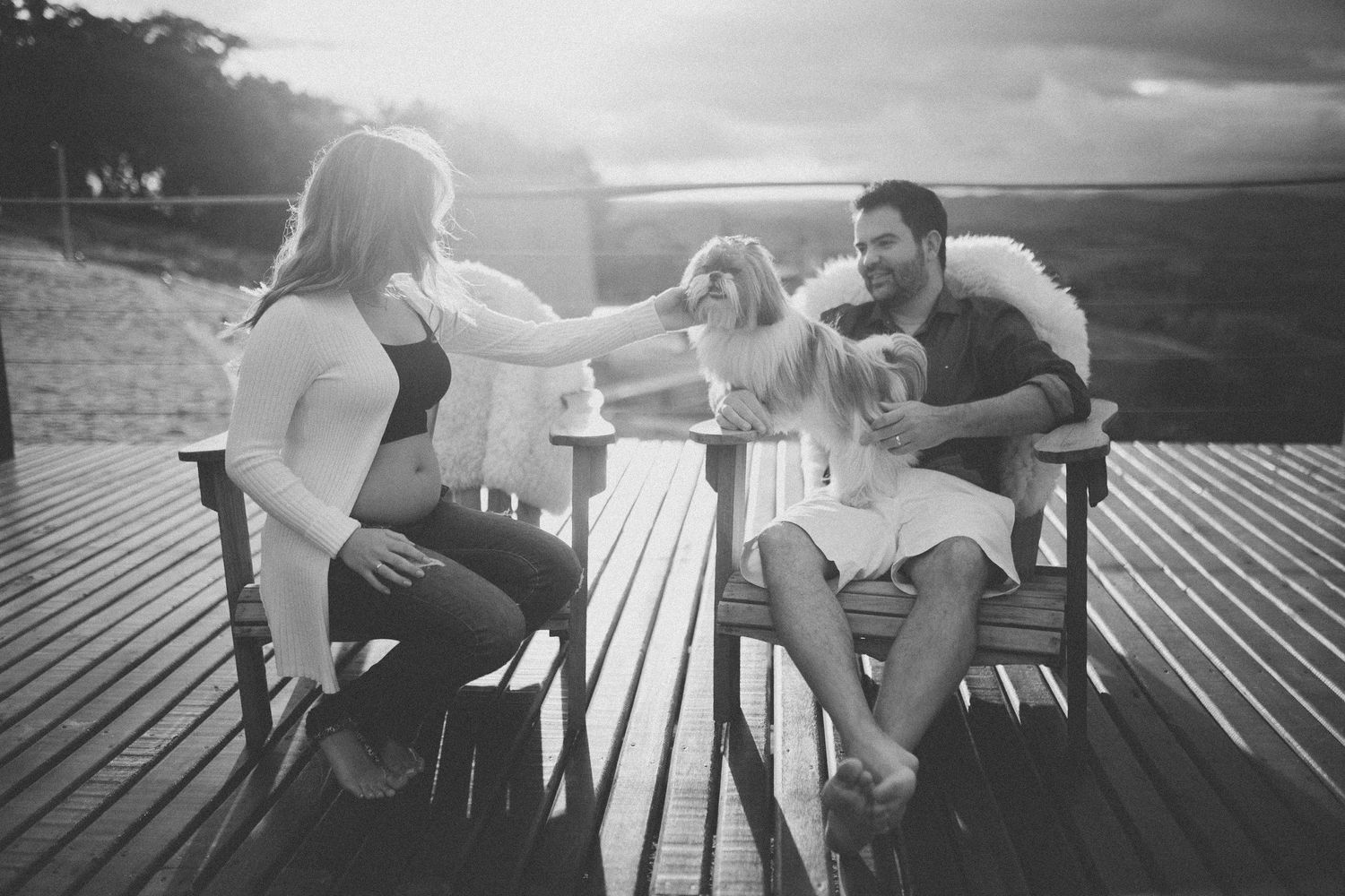 A couple relaxing on wooden deck furniture at sunset with their dog.