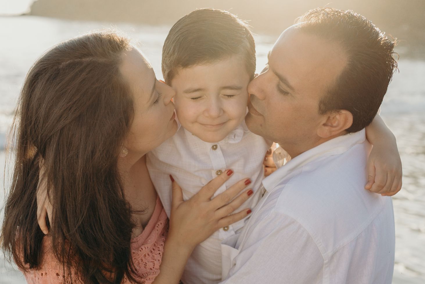 Sweet family embraces during a sunset beach photoshoot in matching pastel outfits.