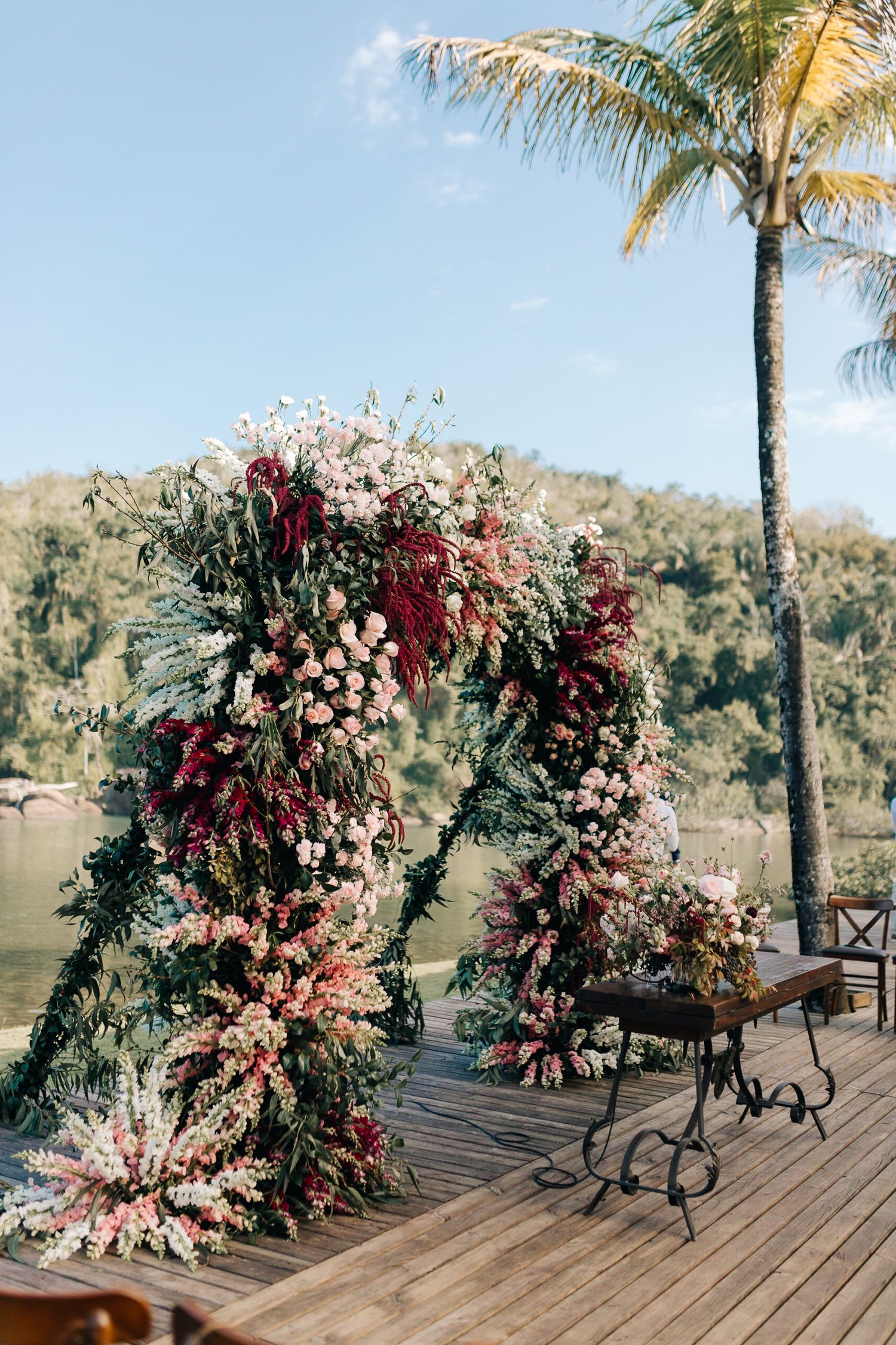 Tropical waterfront wedding setup with lush floral arrangements and palm trees.