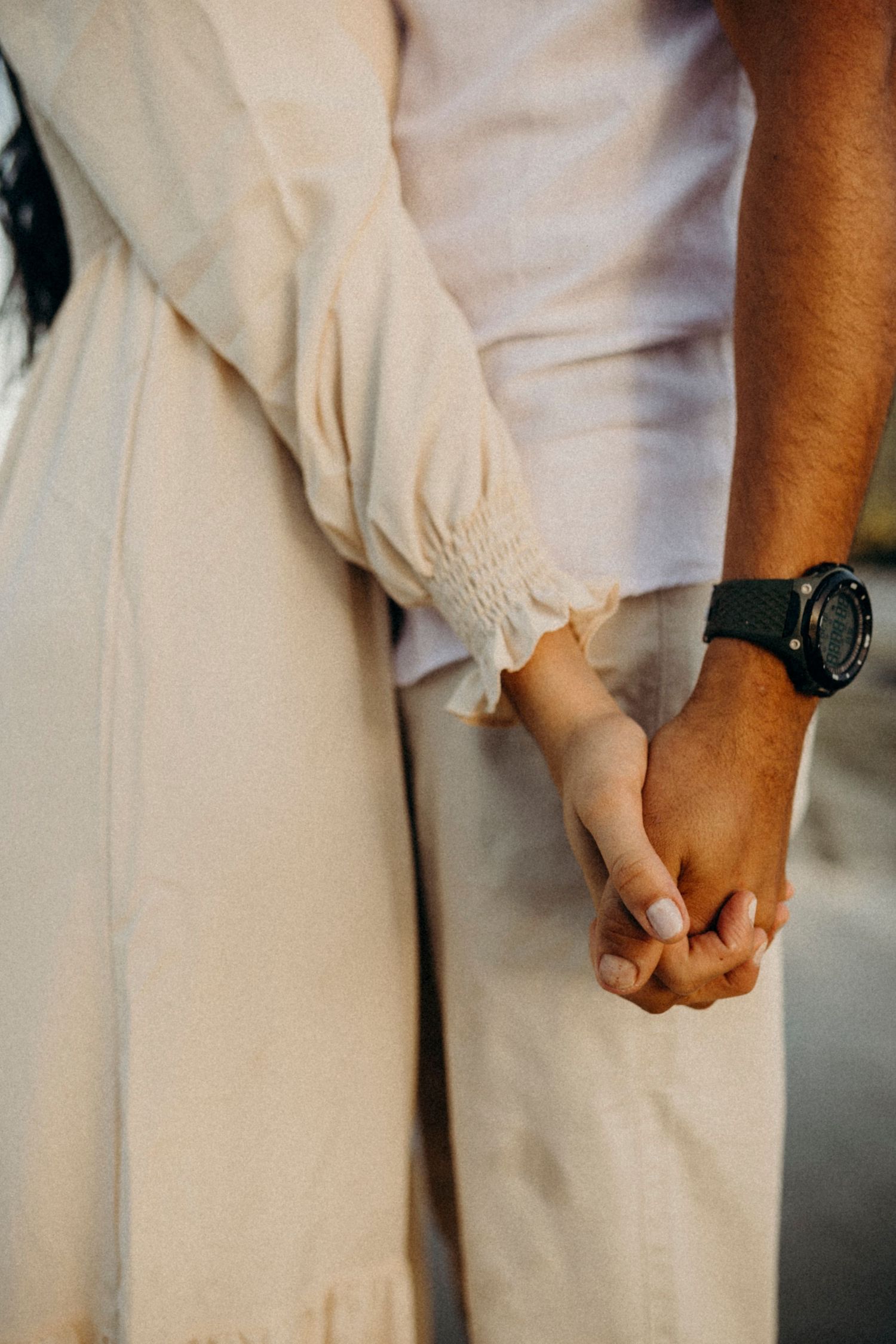 A close-up shot of a couple holding hands while wearing coordinated white outfits.