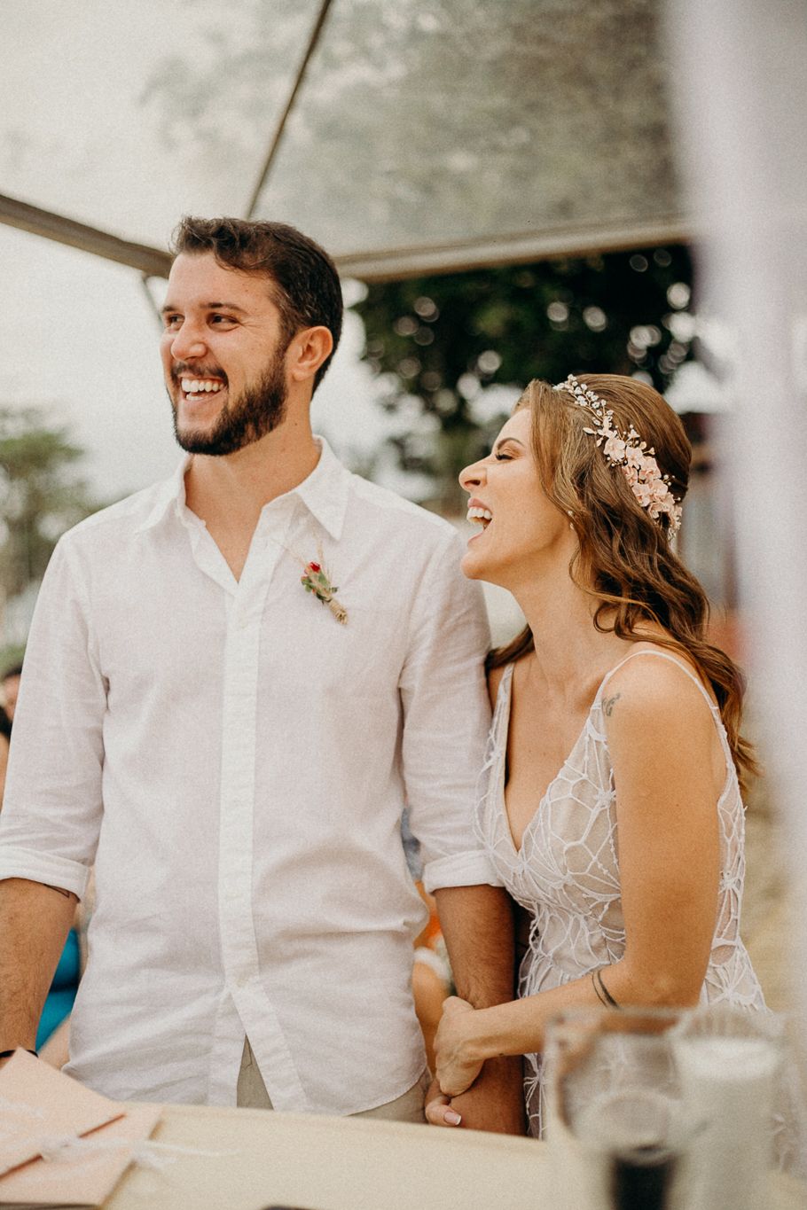 Happy couple shares laughter during outdoor wedding reception under white tent.
