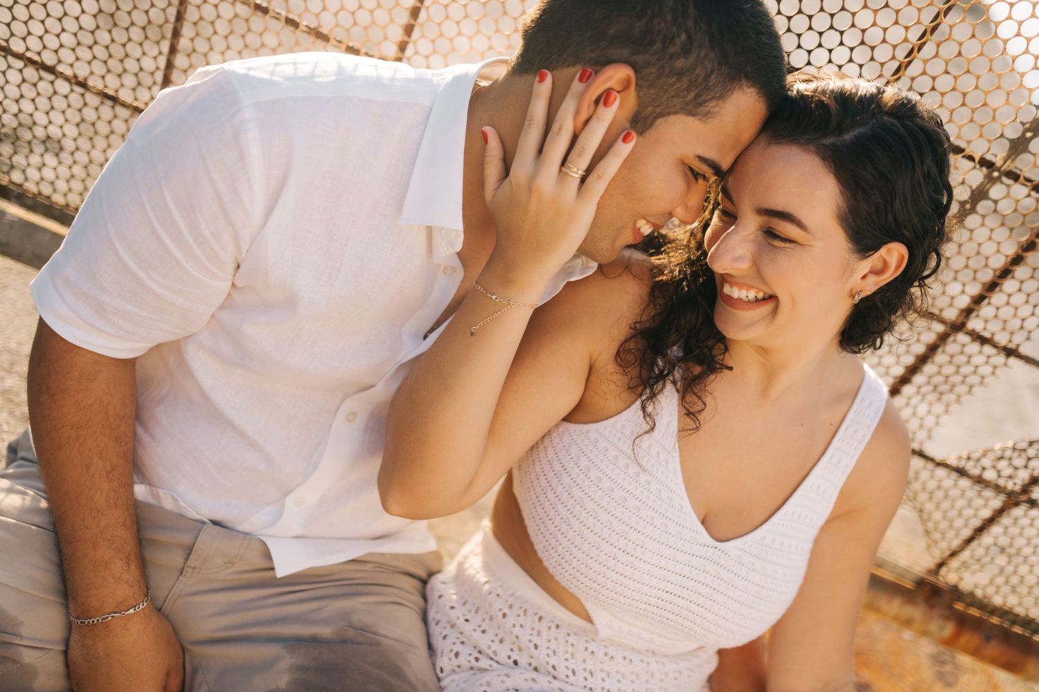 Couple laughing together while sharing a tender moment against a textured wall.