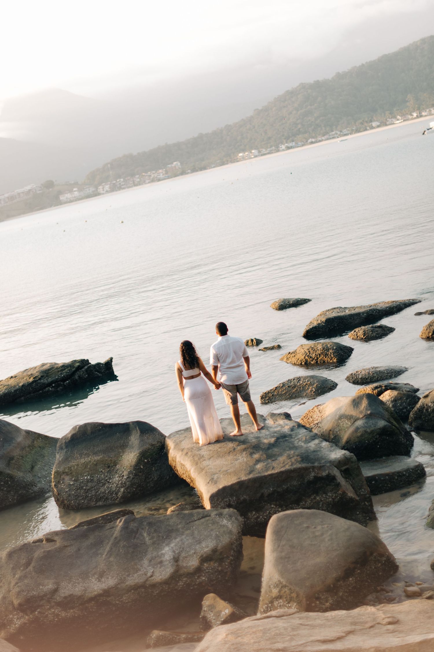 Couple standing together on coastal rocks overlooking misty ocean view.