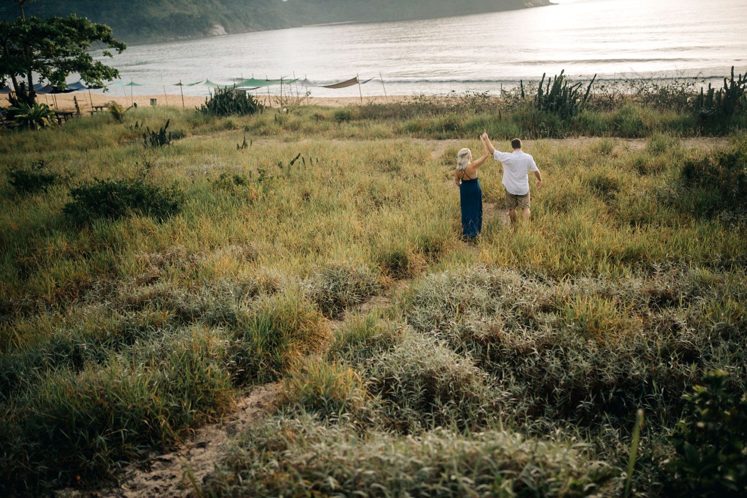 Two figures walking through tall grass with mountains and ocean visible in the distance.