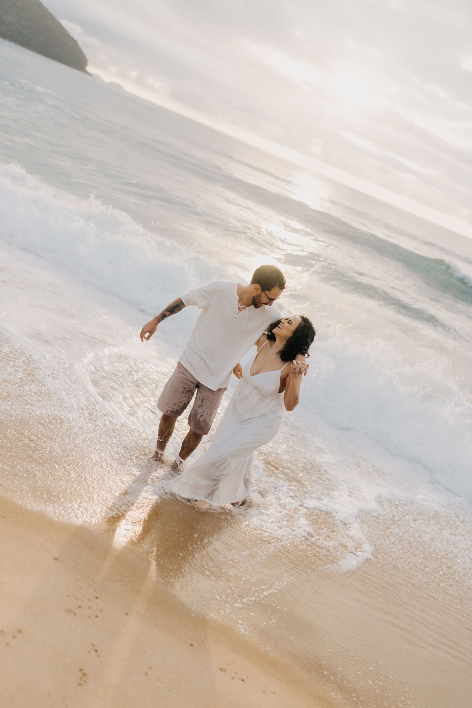 A couple dances in the shallow ocean waves during sunset.