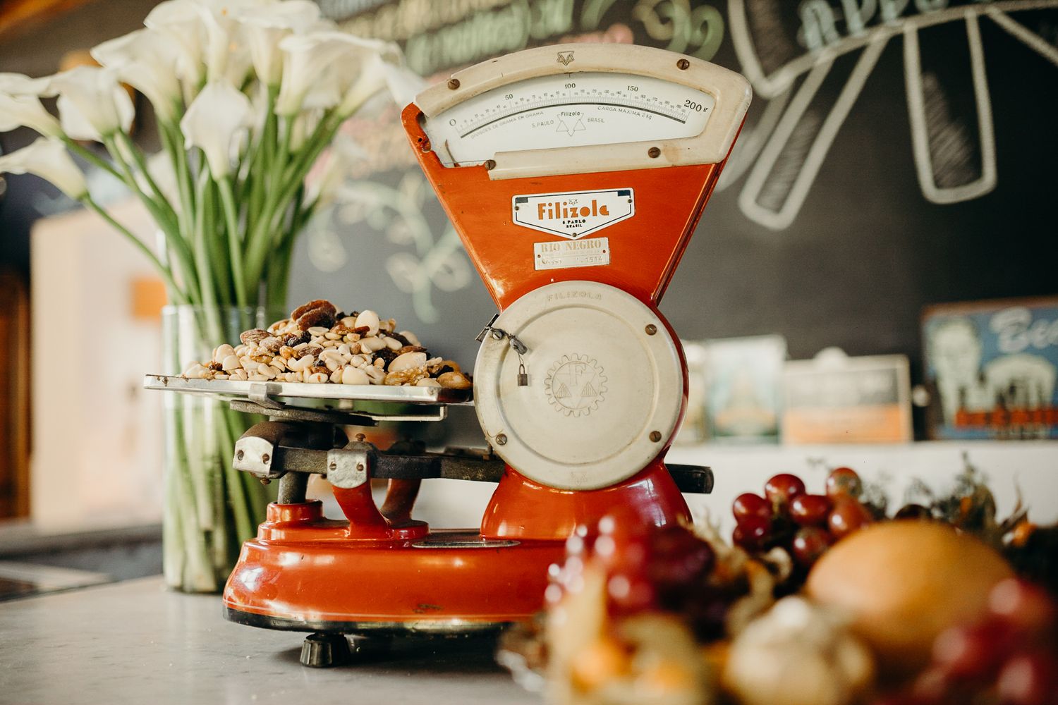 Vintage red kitchen scale with white flowers and fruit displayed on counter.