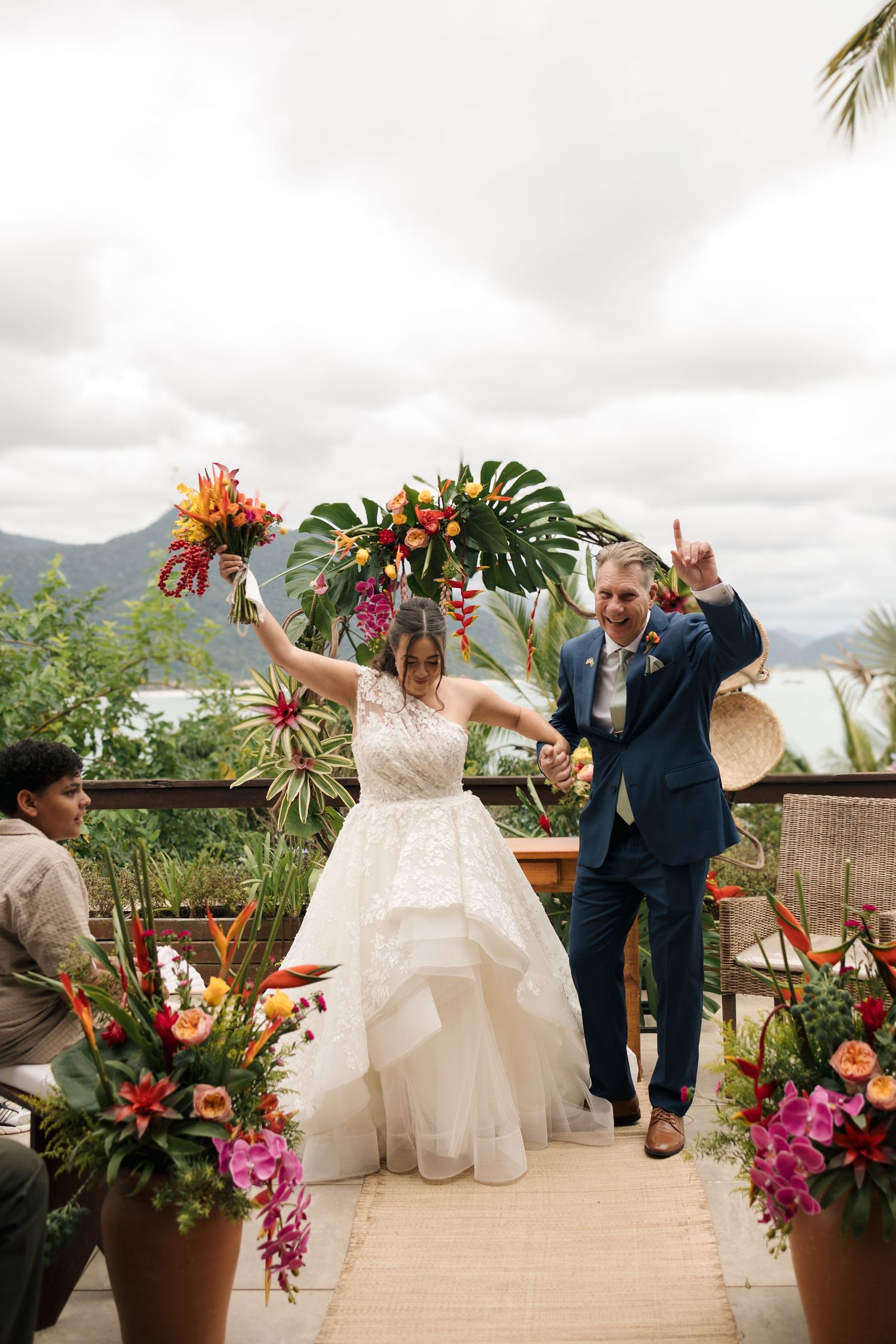 A joyful couple dances on an outdoor terrace decorated with tropical flowers and mountain views in the background.