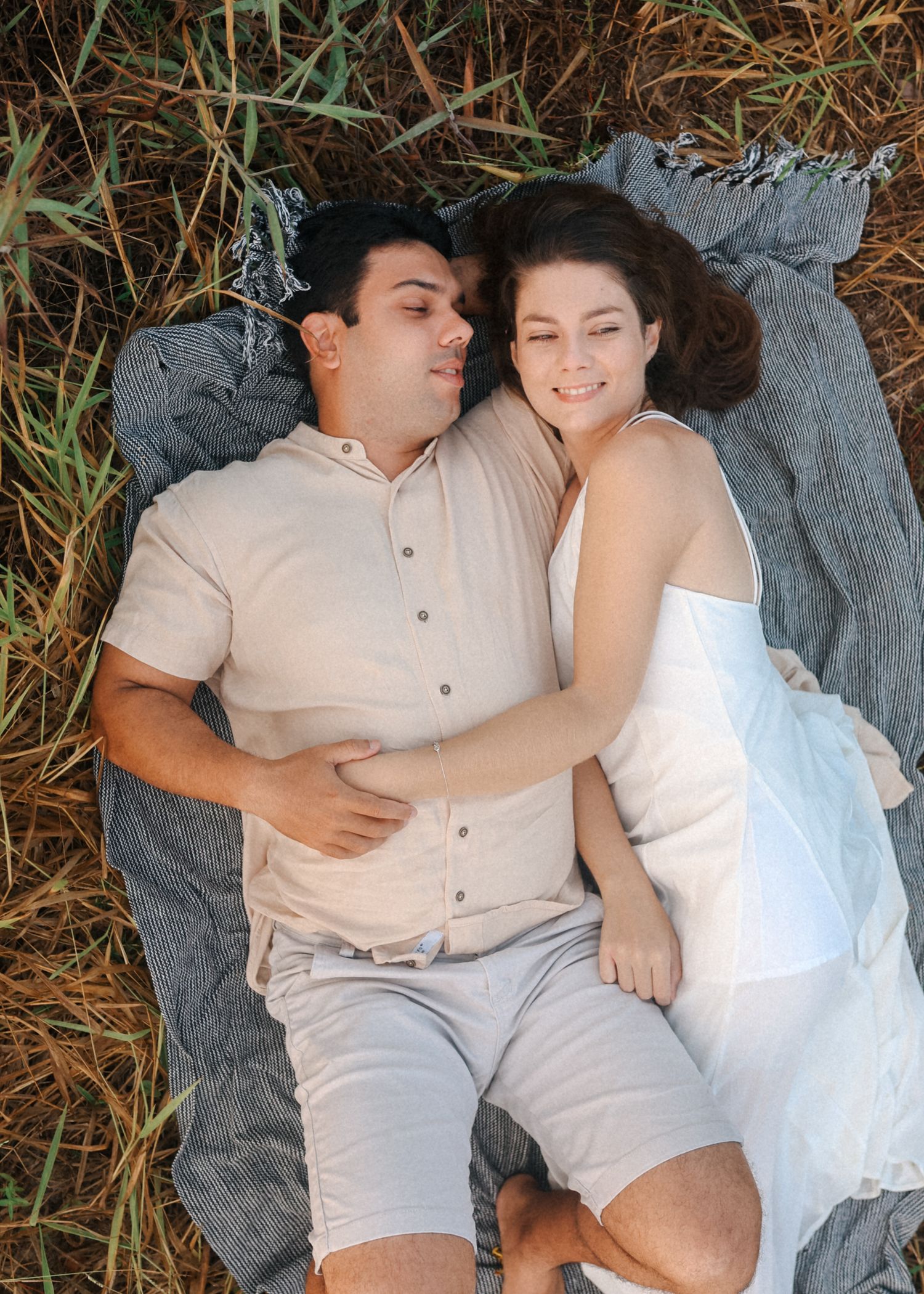 Couple in coordinated white outfits share tender moments on a blanket outdoors.