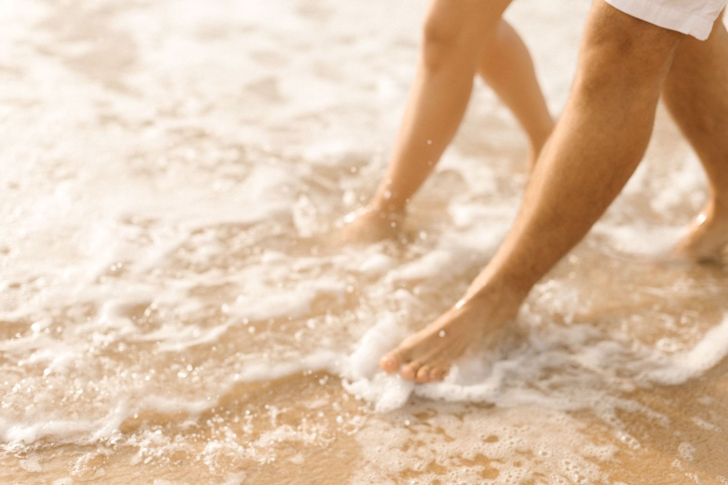 Feet splashing in gentle ocean waves on a sunny beach.
