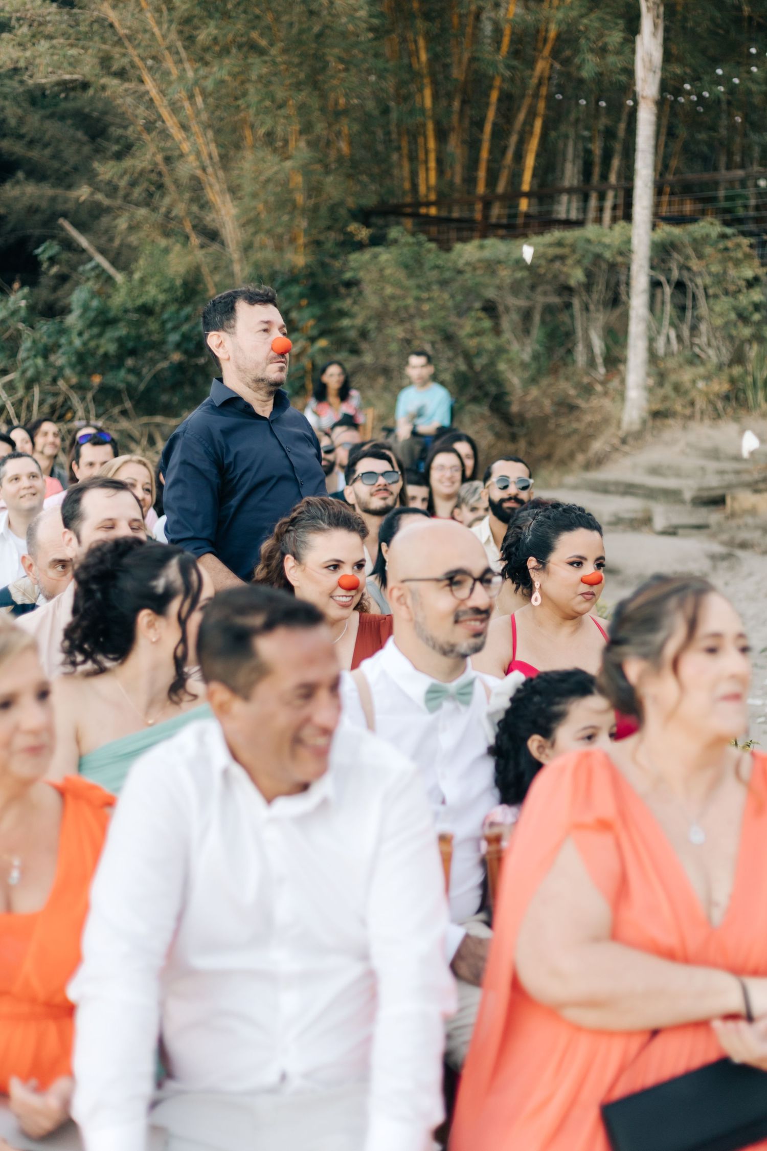 Crowd of wedding guests in coral dresses and white shirts watch the ceremony.