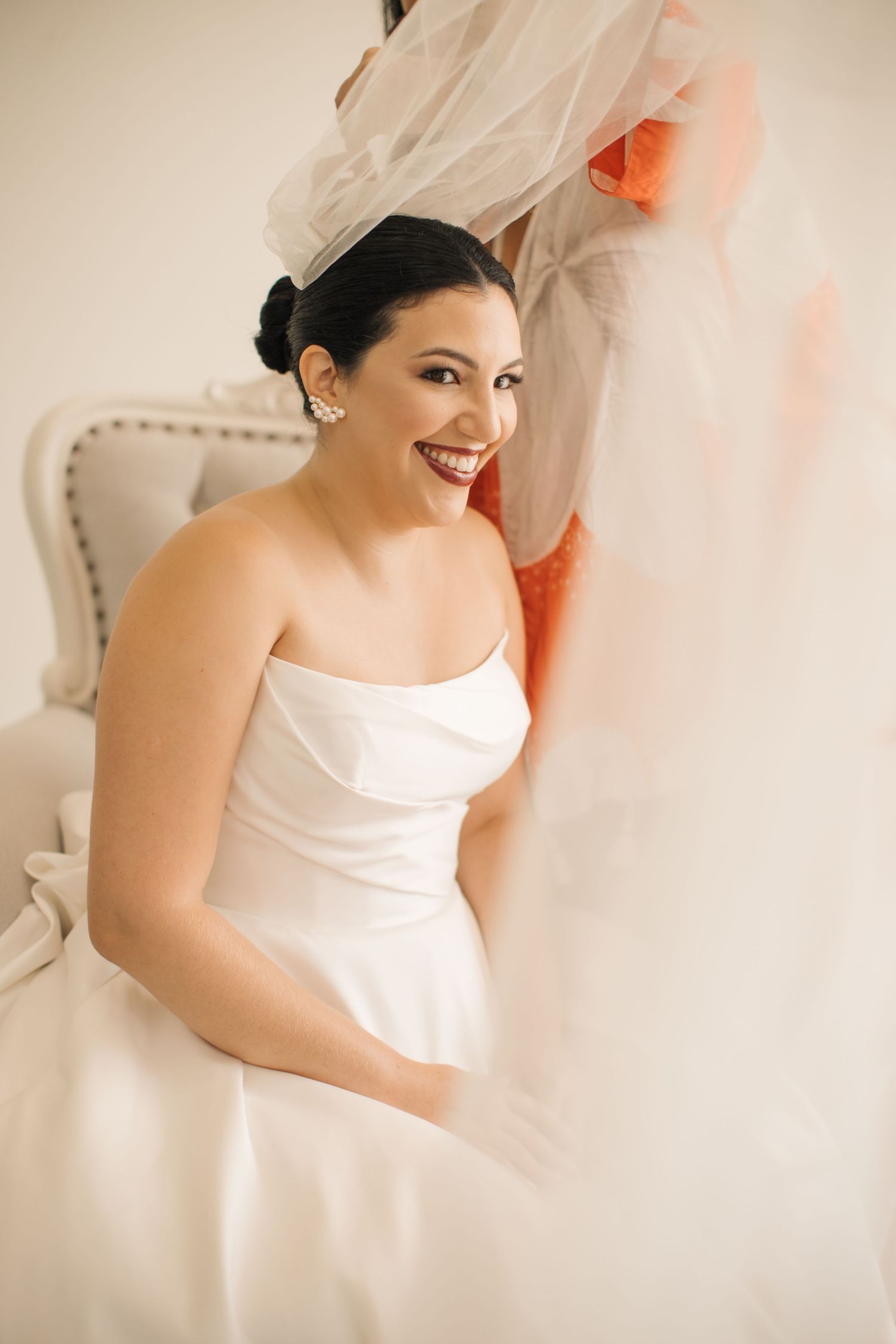 Joyful candid moment during wedding preparations with white gown and natural lighting.