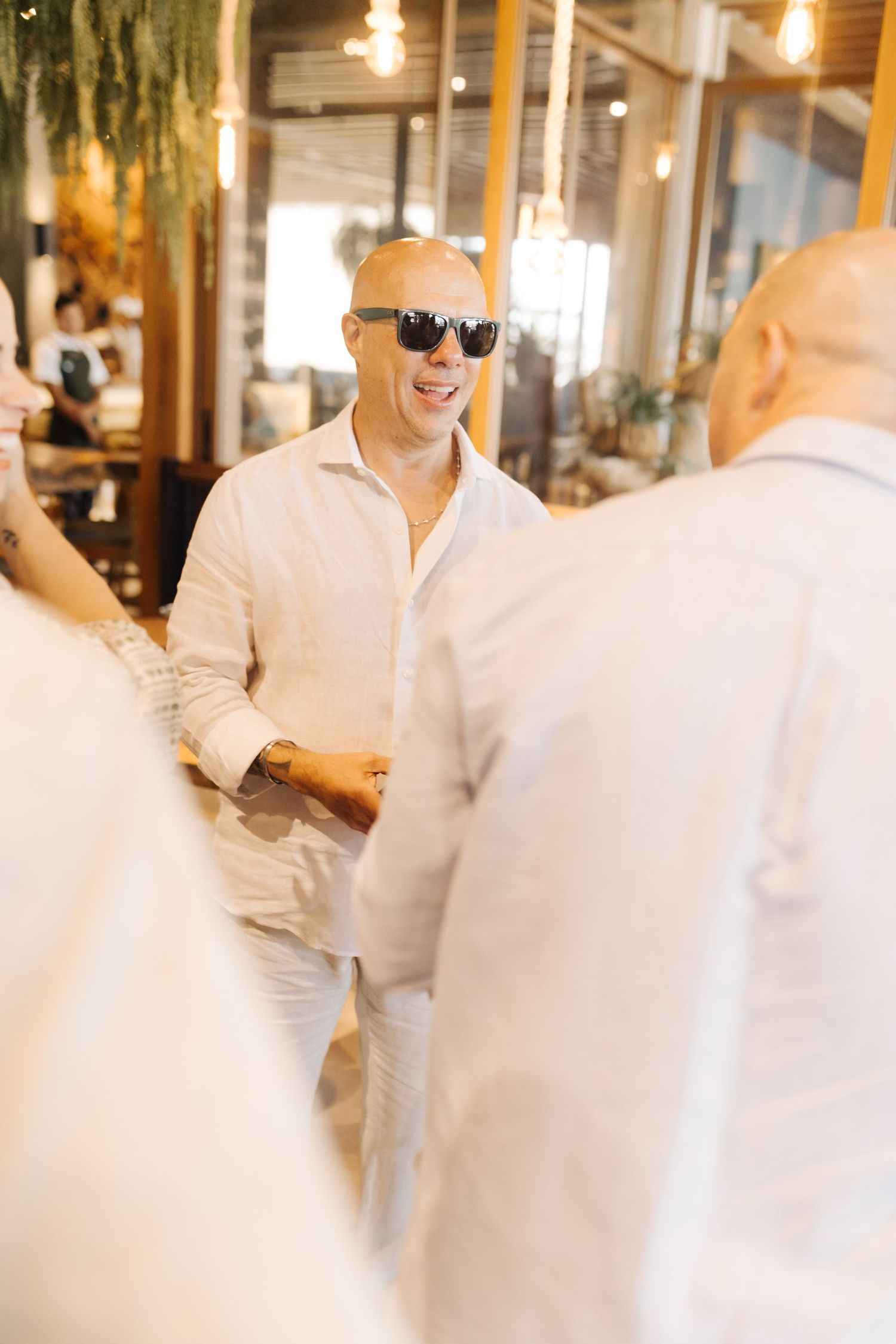 Wedding guest in white attire and sunglasses socializing at indoor venue.