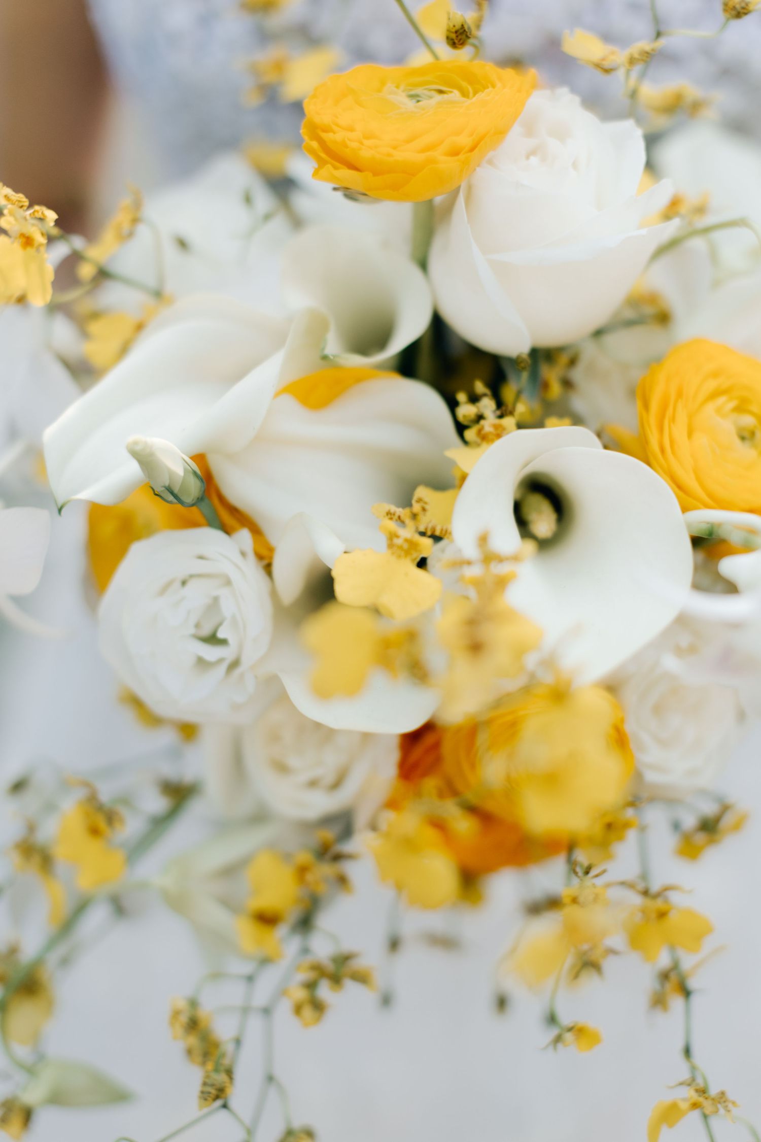 Elegant wedding bouquet featuring white calla lilies and yellow ranunculus with delicate small flowers.