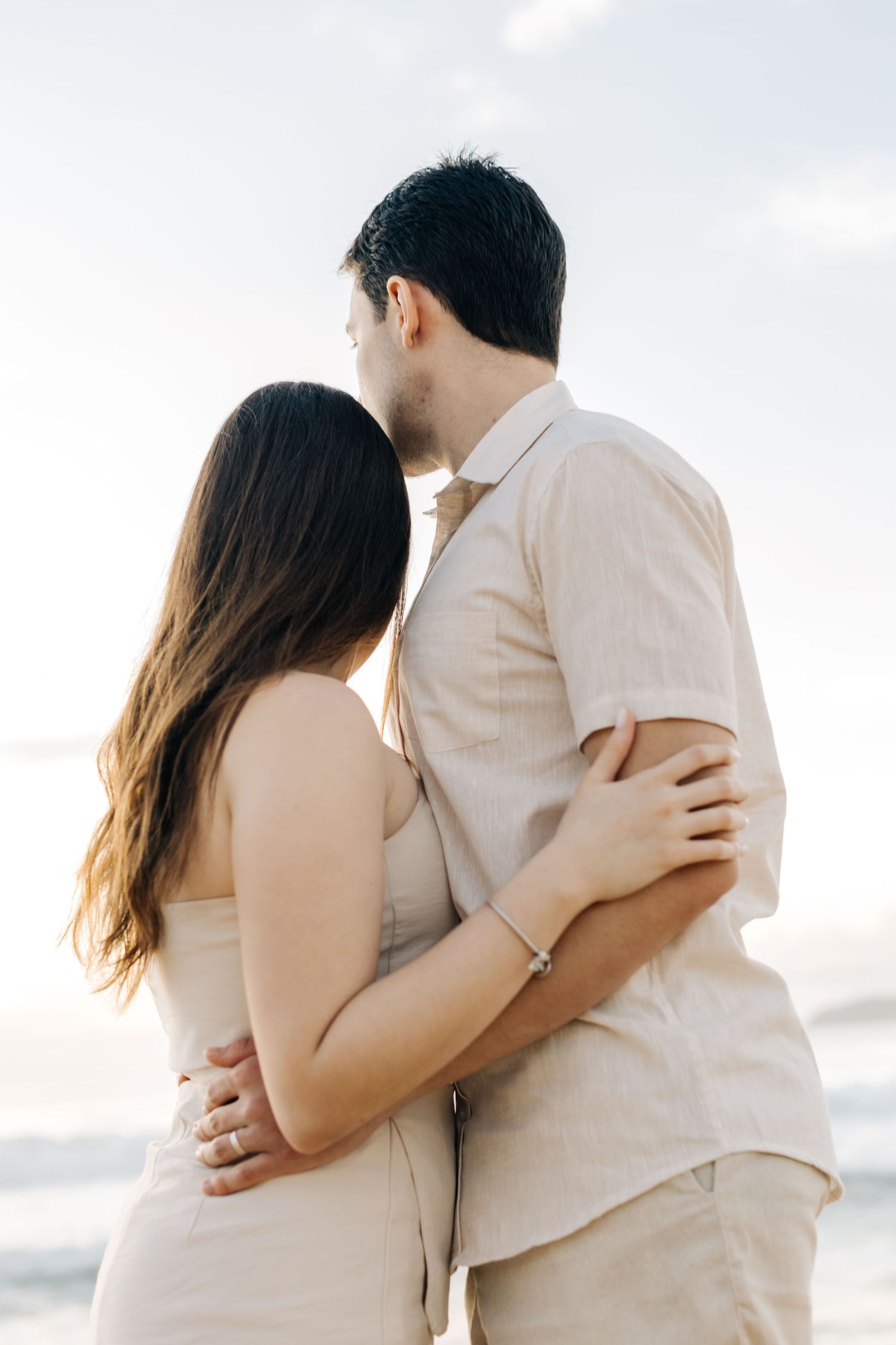 Side view of a couple in matching beige outfits embracing on a sunny beach.
