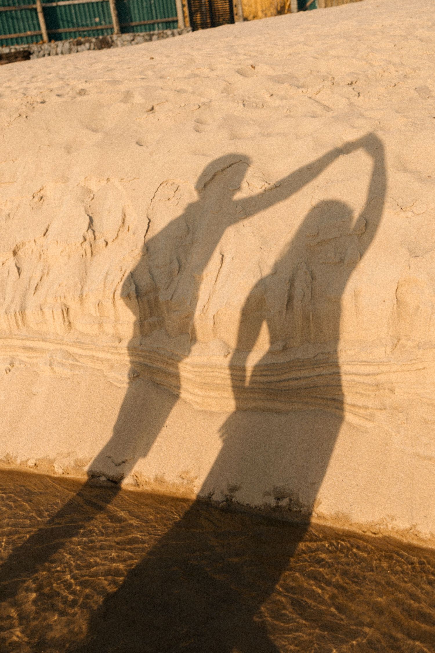 A sequence of shadow silhouettes cast on a beige wall show two people playfully posing and dancing together.
