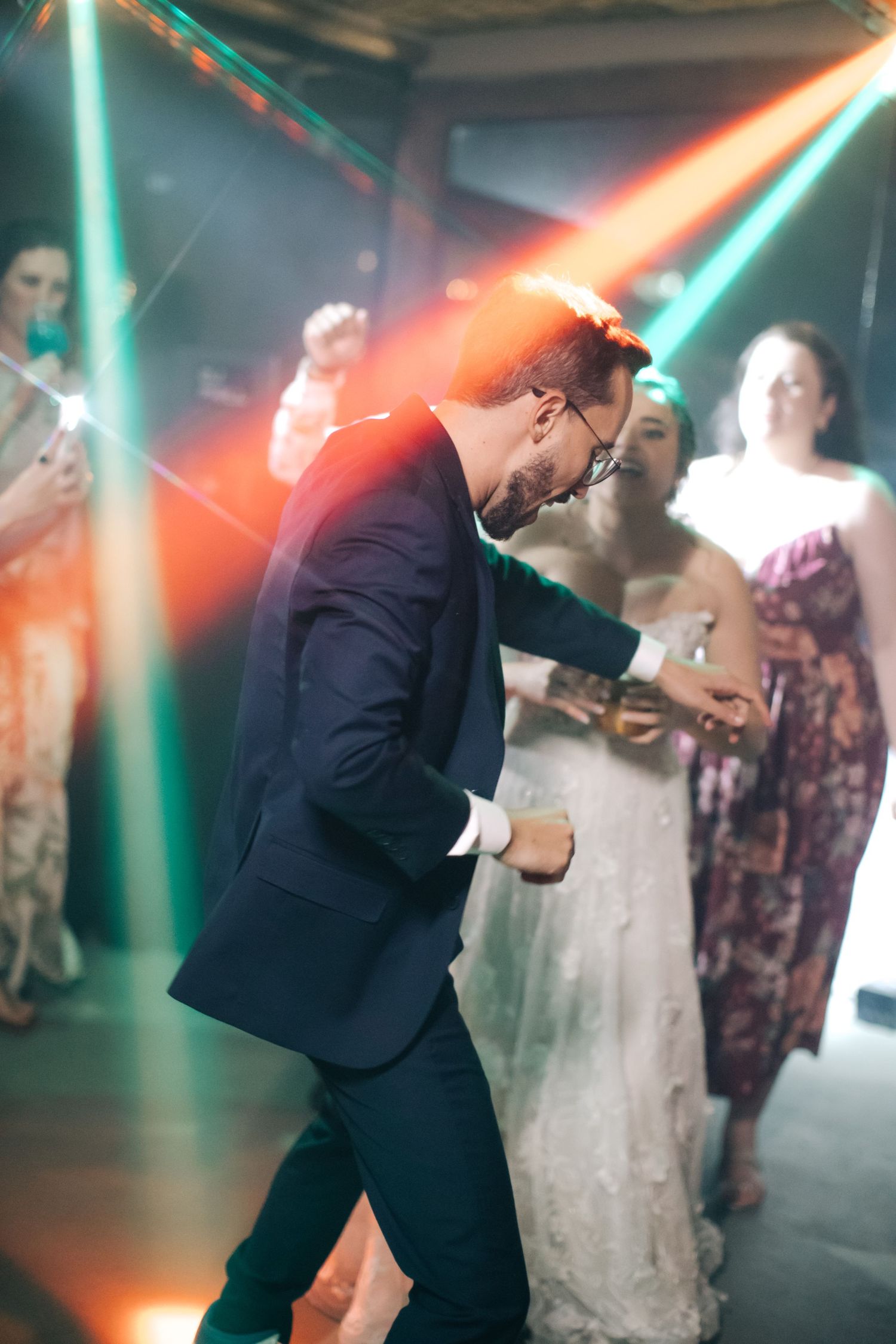 A lively dance moment at a wedding reception illuminated by green and red spotlights.