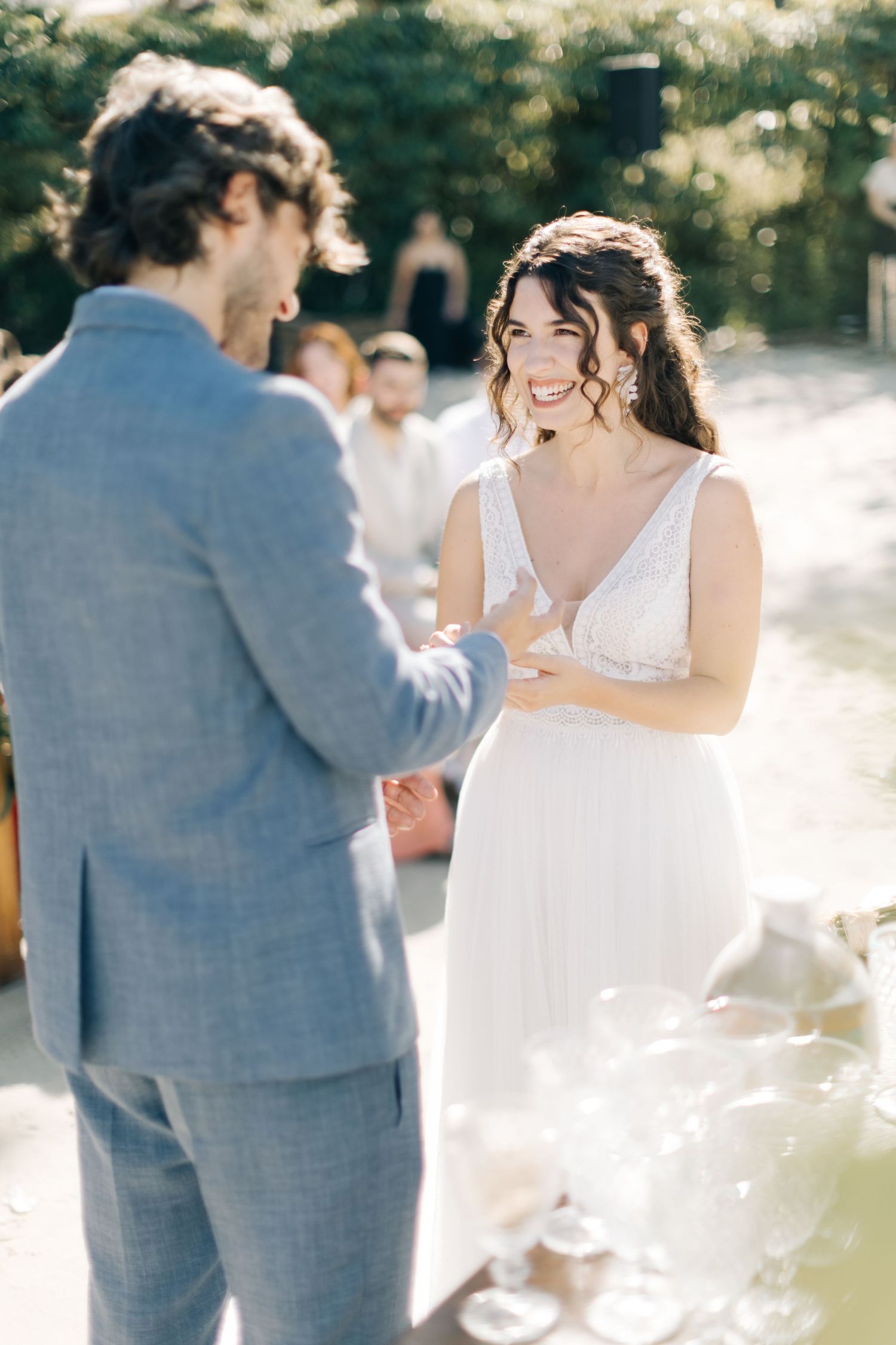 Couple exchanges vows during an outdoor wedding ceremony with sunlit forest backdrop.