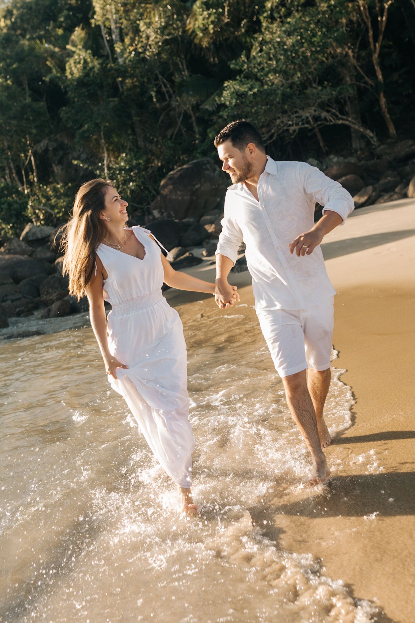 Group playing and splashing in ocean waves while wearing all white clothing.