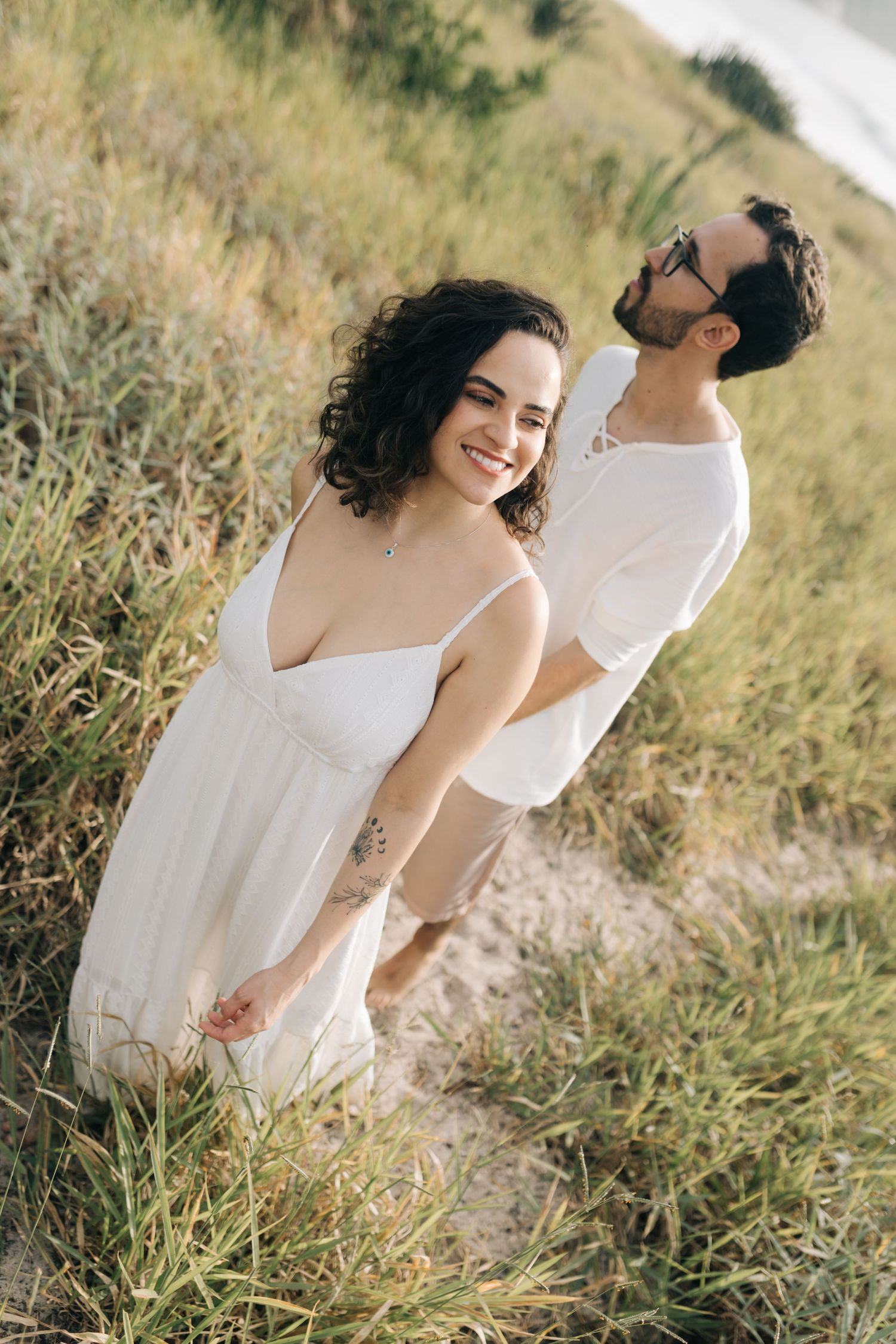 Happy couple walking together through golden grass field by the coast.