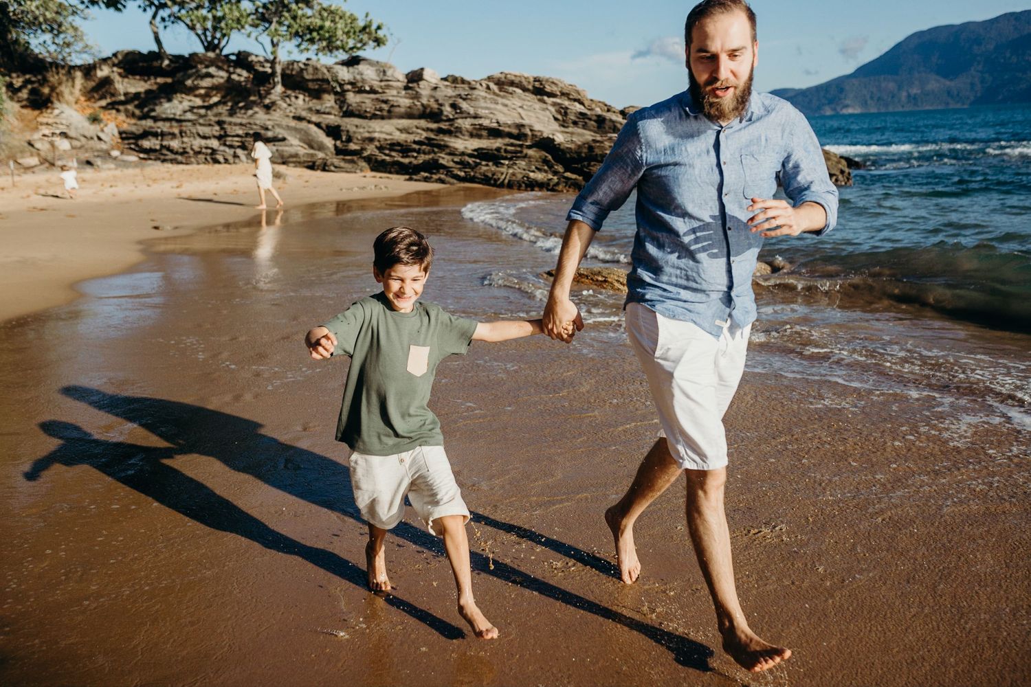 Family walking and playing together along rocky beach shoreline.