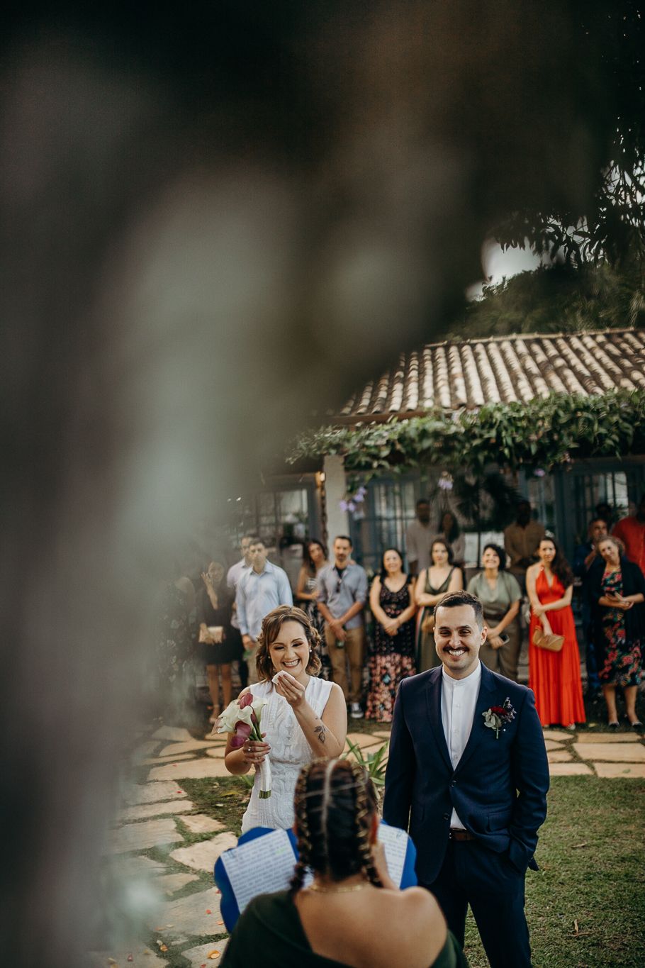 Wedding ceremony unfolds in a garden setting with natural greenery and stone paths.