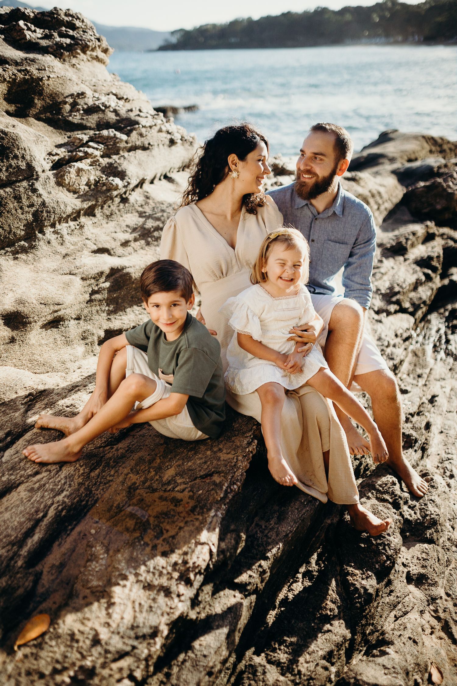 A family shares joyful moments together while sitting on coastal rocks during golden hour at the beach.