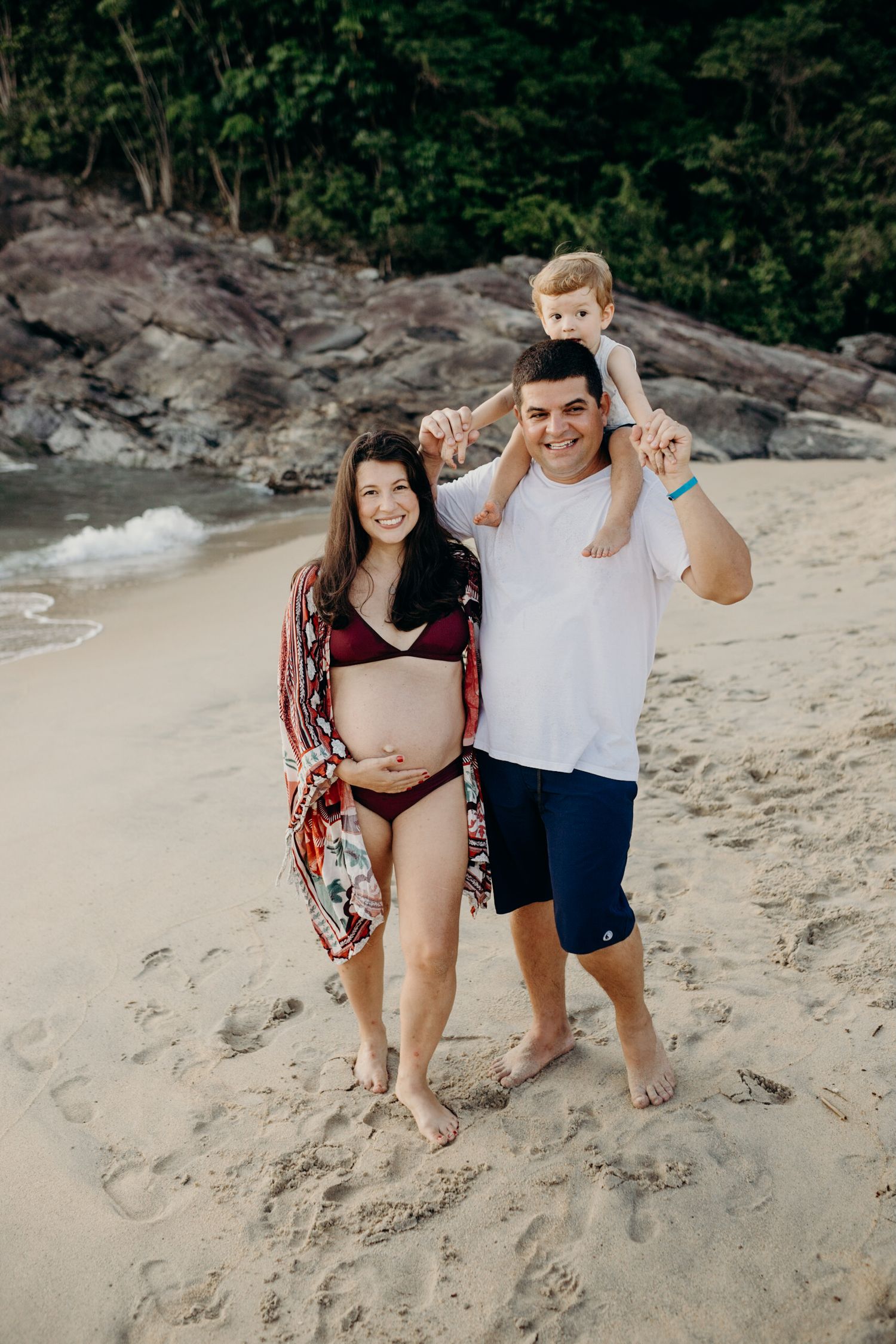 Family portrait on a beautiful beach with volcanic rocks and dense tropical foliage.