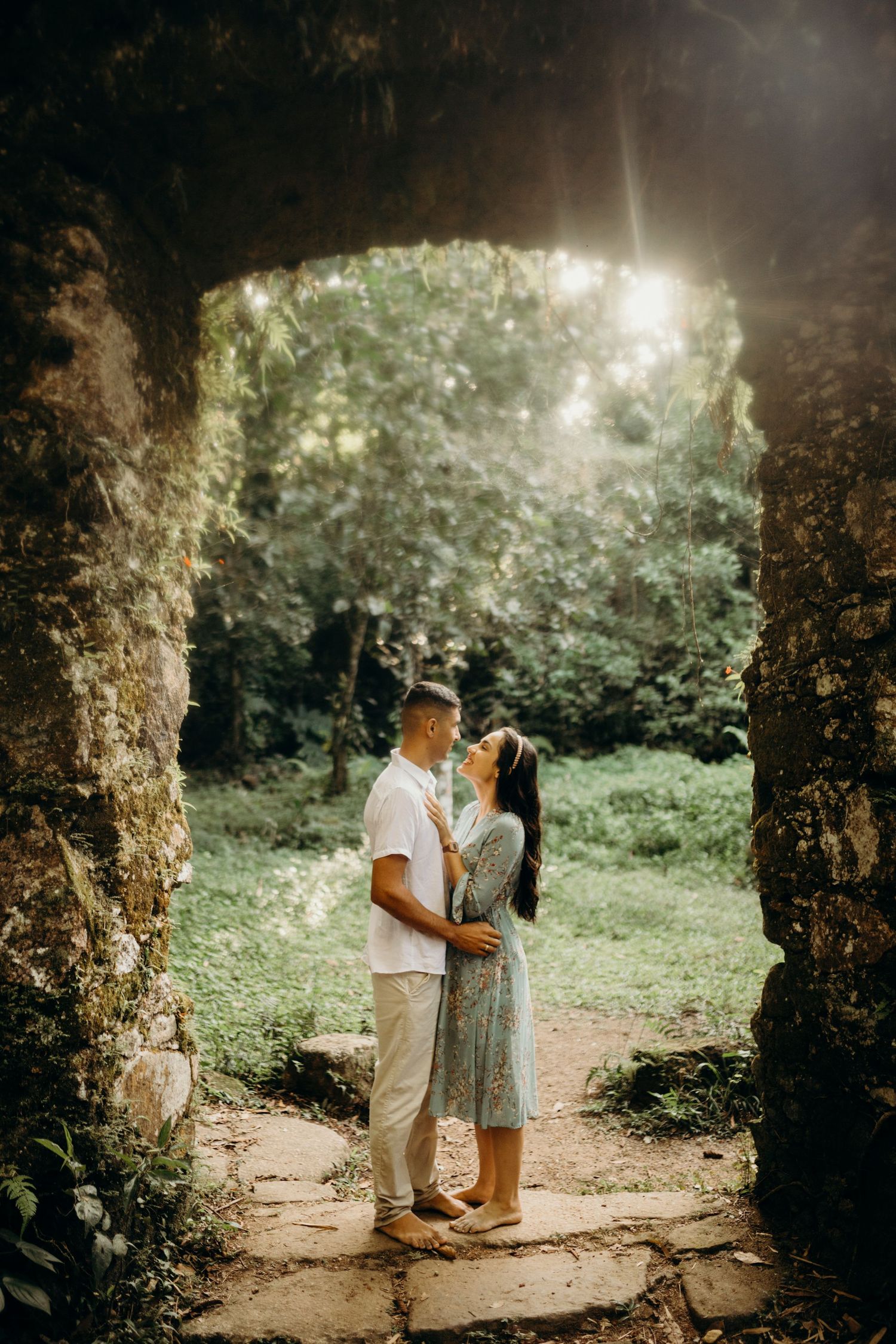 Couple sharing an intimate moment framed by ancient stone ruins with sunlight streaming through.