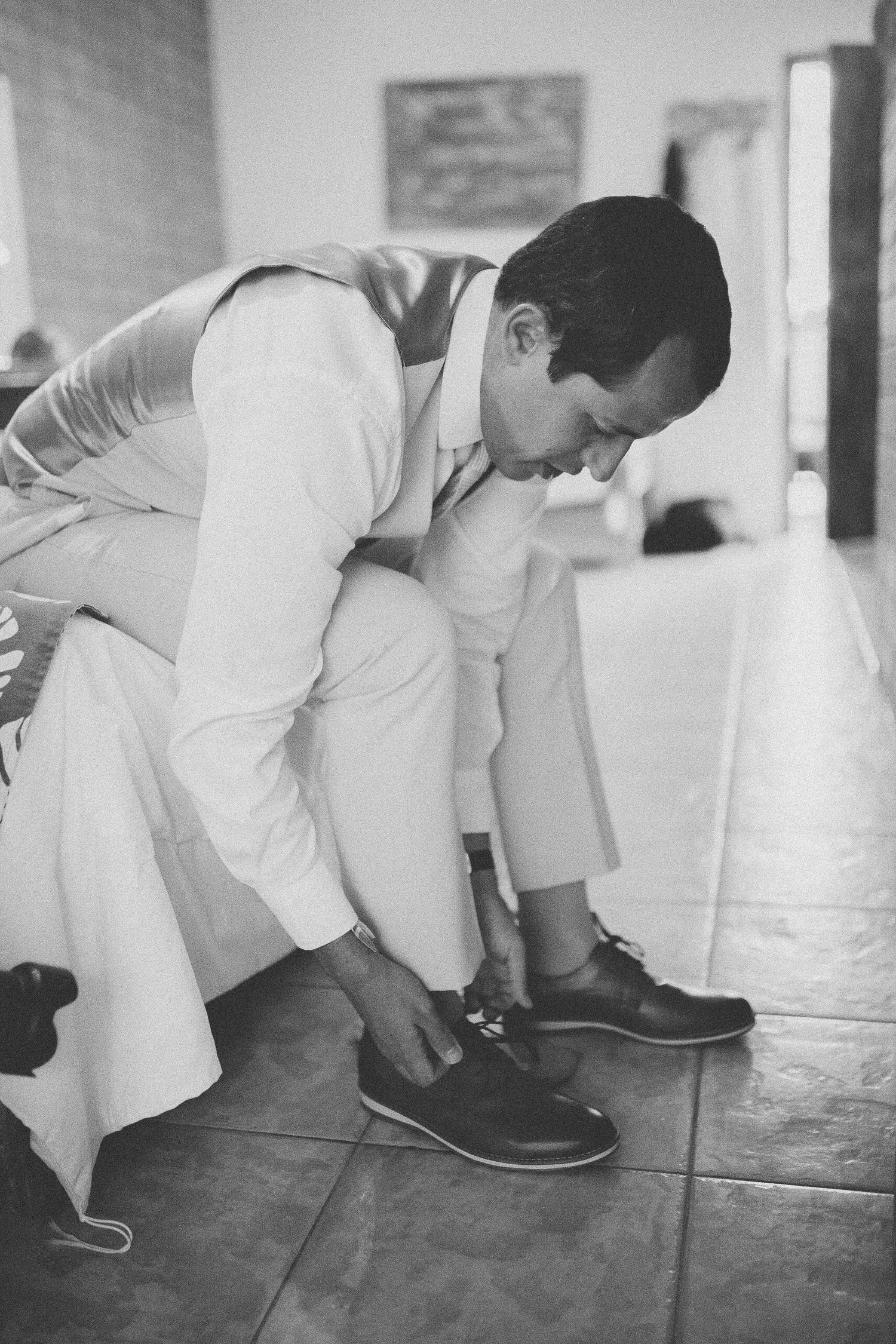Person in formal attire bends down to tie dress shoes on tiled floor.