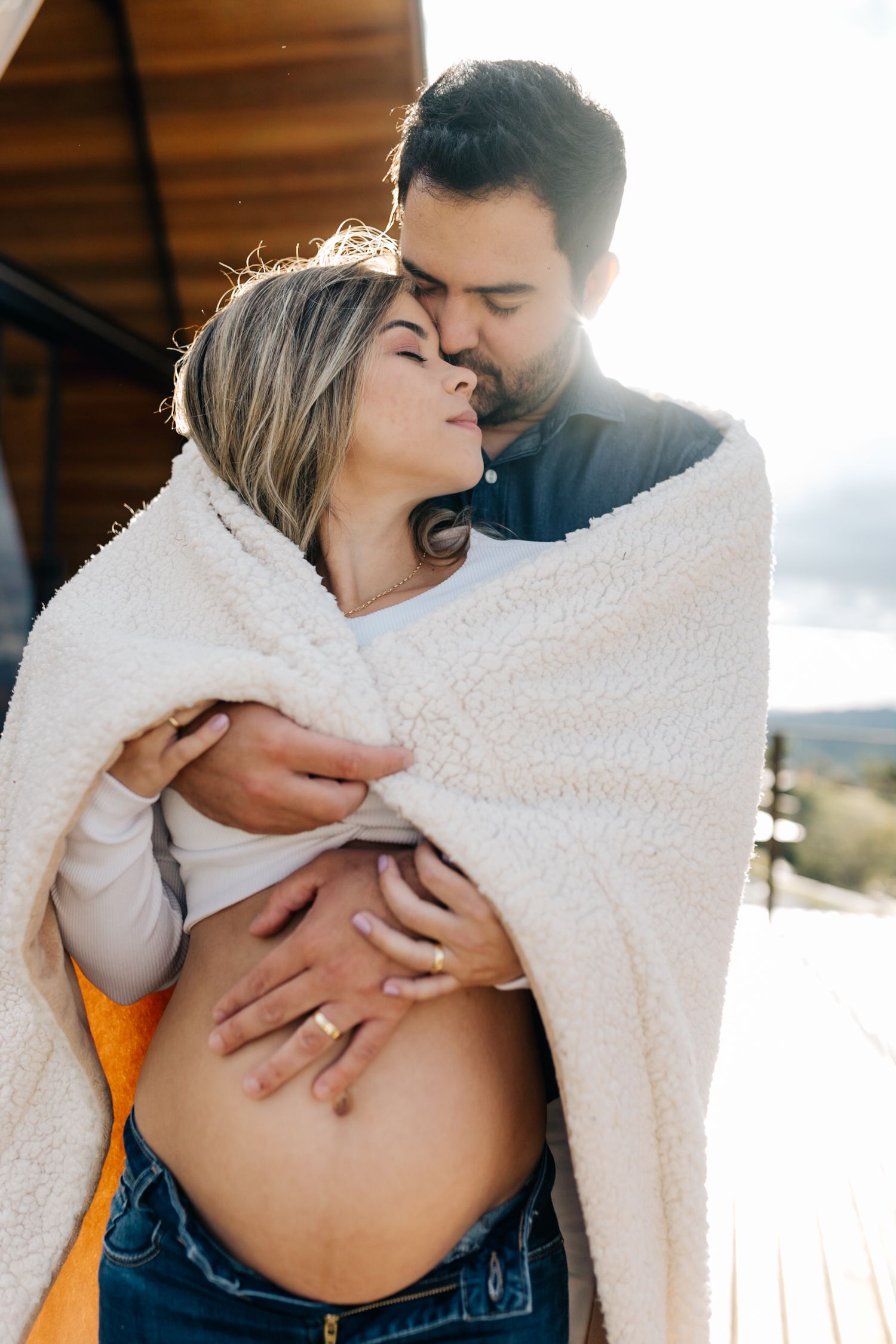 Close-up maternity photos showing gentle moments between a couple wrapped in a cozy white blanket.