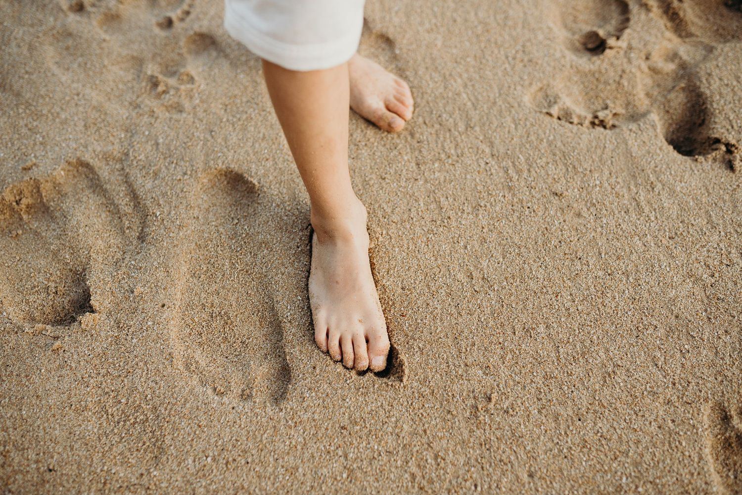 Child's bare feet making impressions in beach sand.