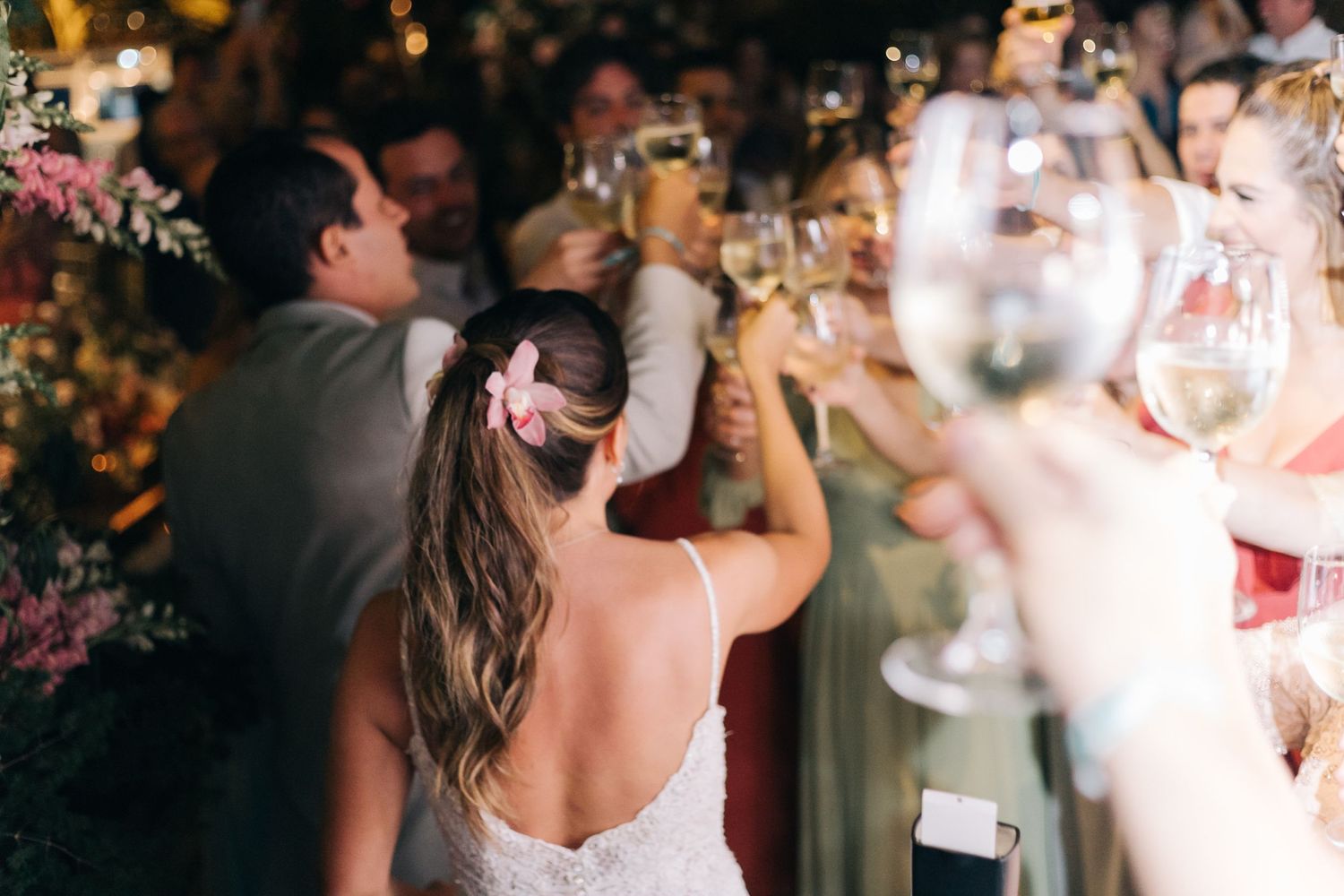 Wedding reception guests raising glasses in celebration during an evening toast.