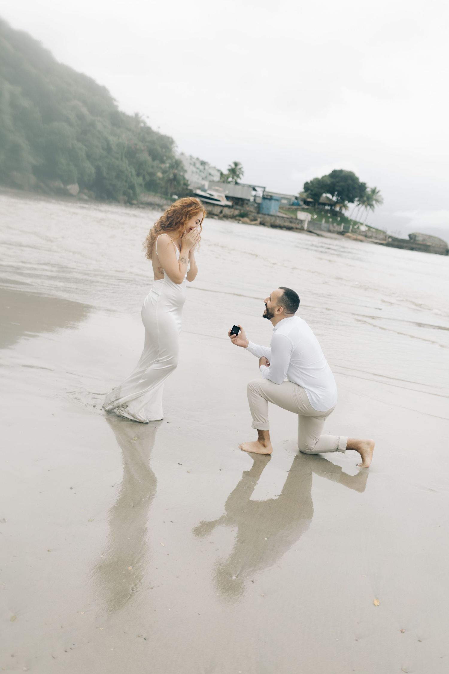 Beach proposal photography with surprised reaction and coastal backdrop.