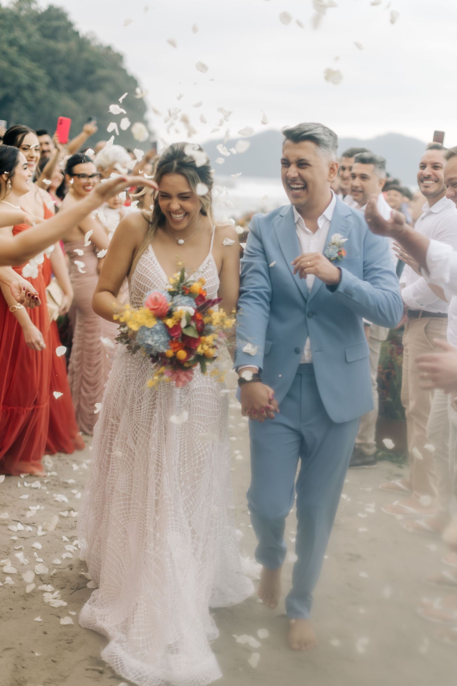 Wedding celebration with confetti toss on sandy beach surrounded by guests.